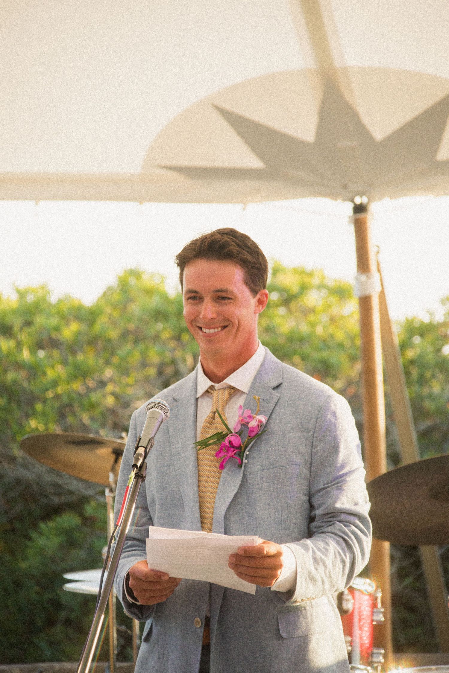 A speaker delivers remarks at a wedding reception podium under a white tent.
