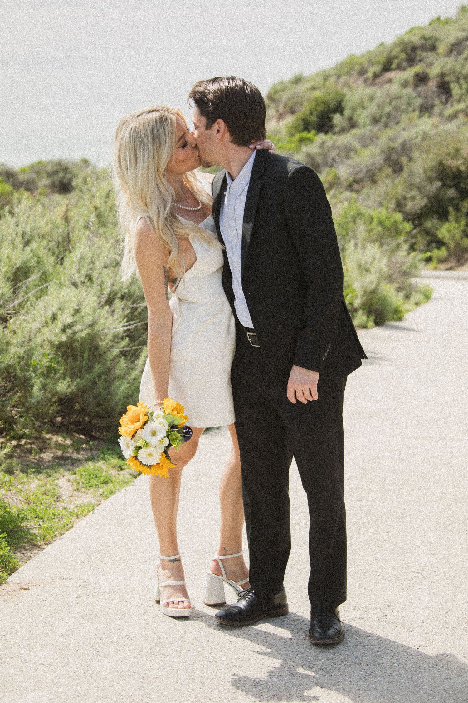 Romantic wedding portraits on scenic coastal trail with natural vegetation.