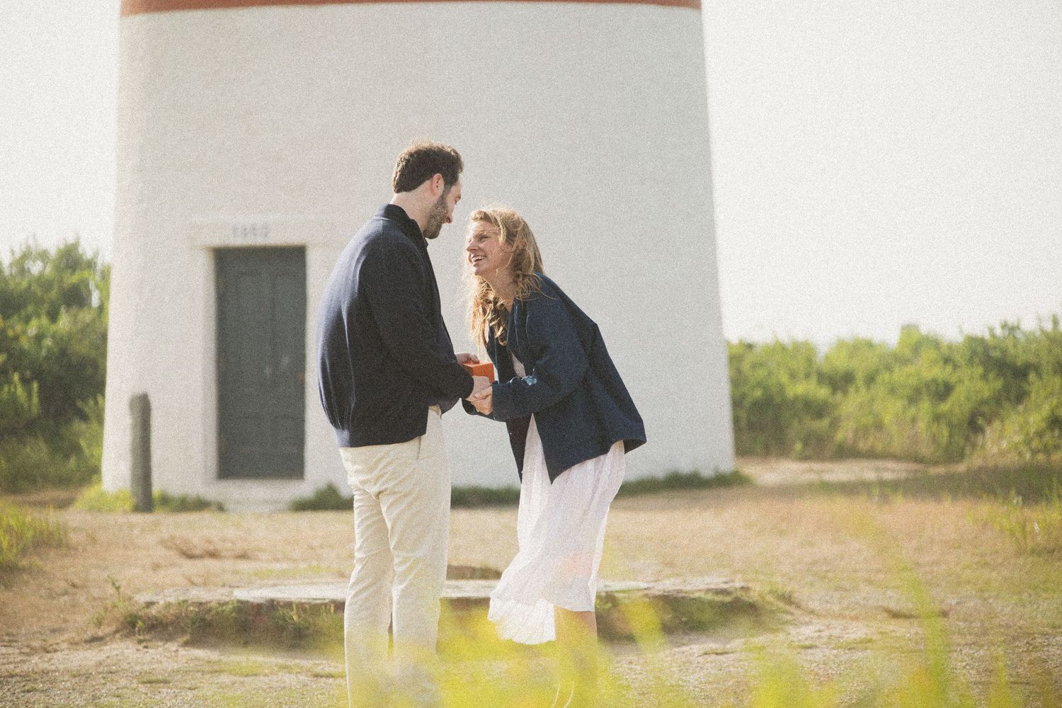 Couple sharing intimate moment by lighthouse wall in afternoon sunlight.