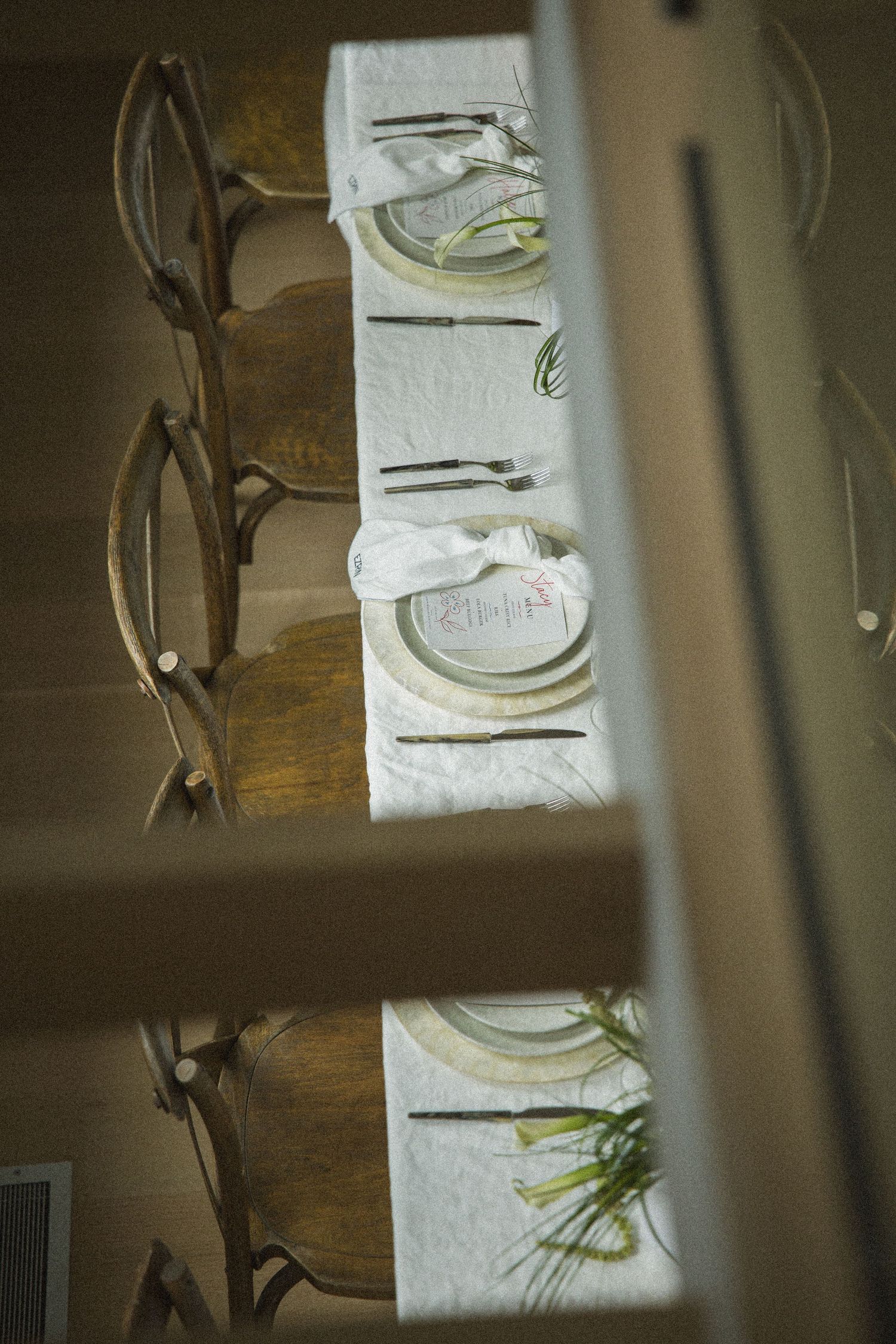 Elegant dining table set with white linen, gold plates, and wooden chairs viewed from above.