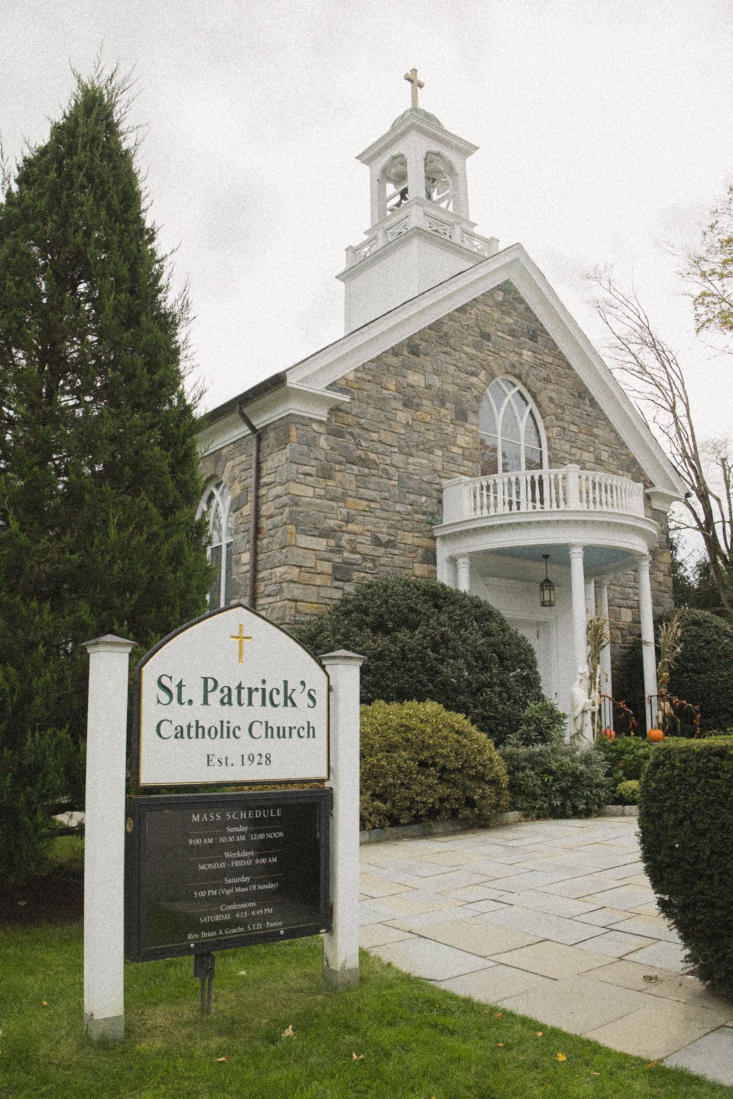 St. Patrick's Catholic Church sign in front of a stone church with a white bell tower, cross, and columned entrance.