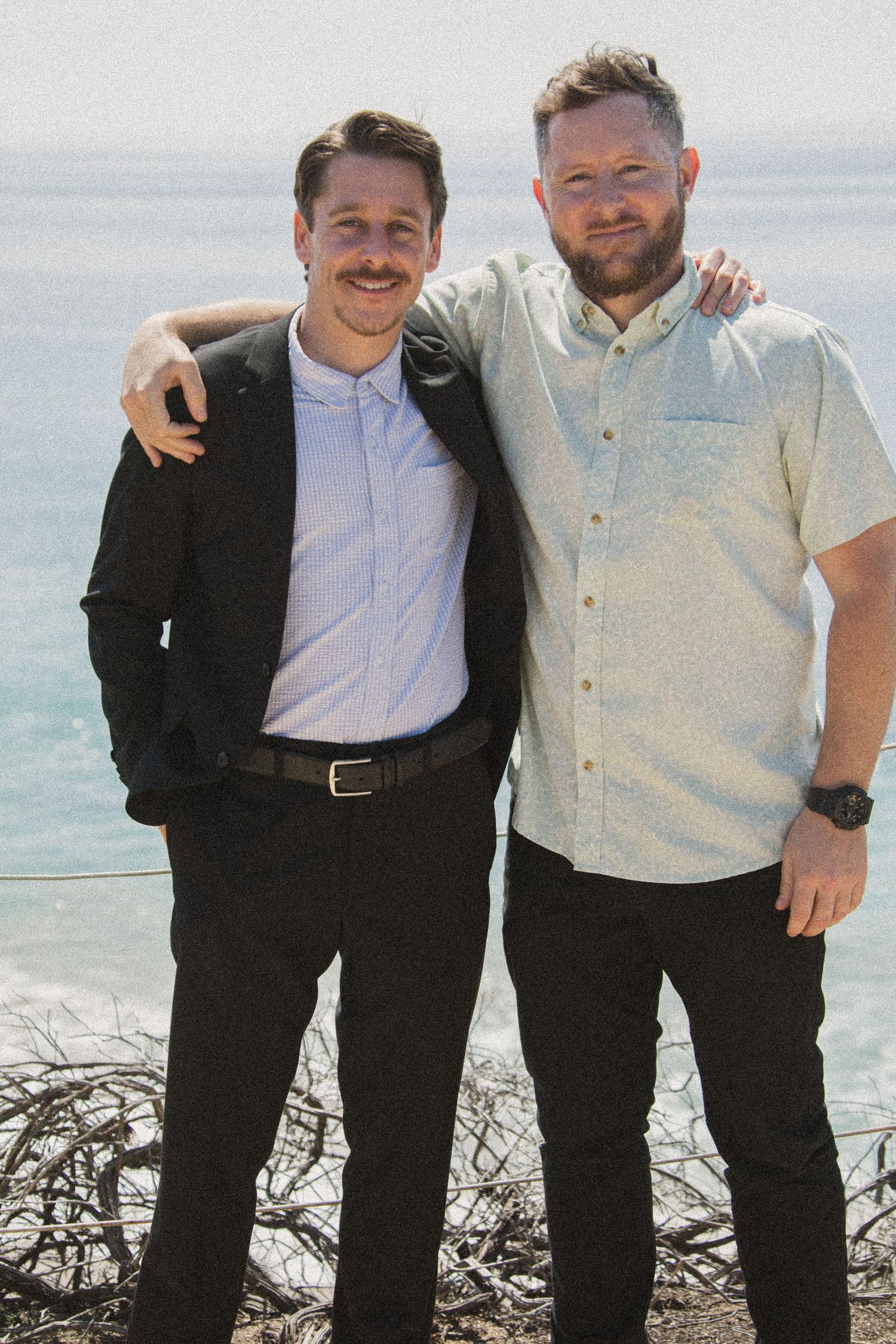 Men in dark and light colored formal wear posing together with ocean backdrop.