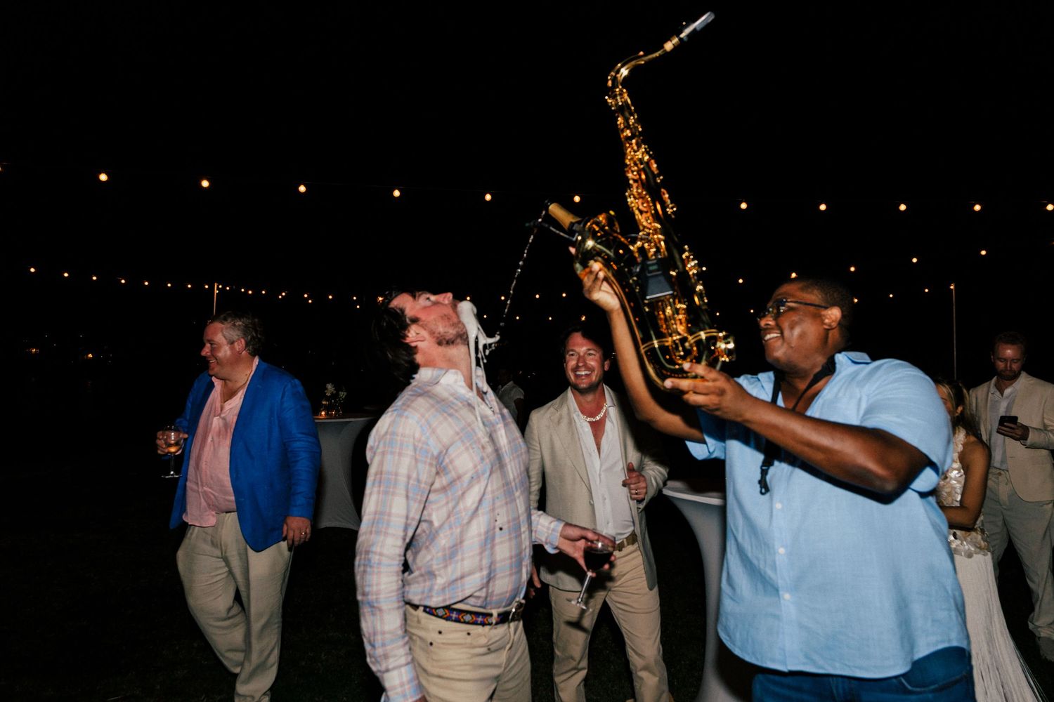 Party guests dancing and celebrating under string lights at a nighttime outdoor event.