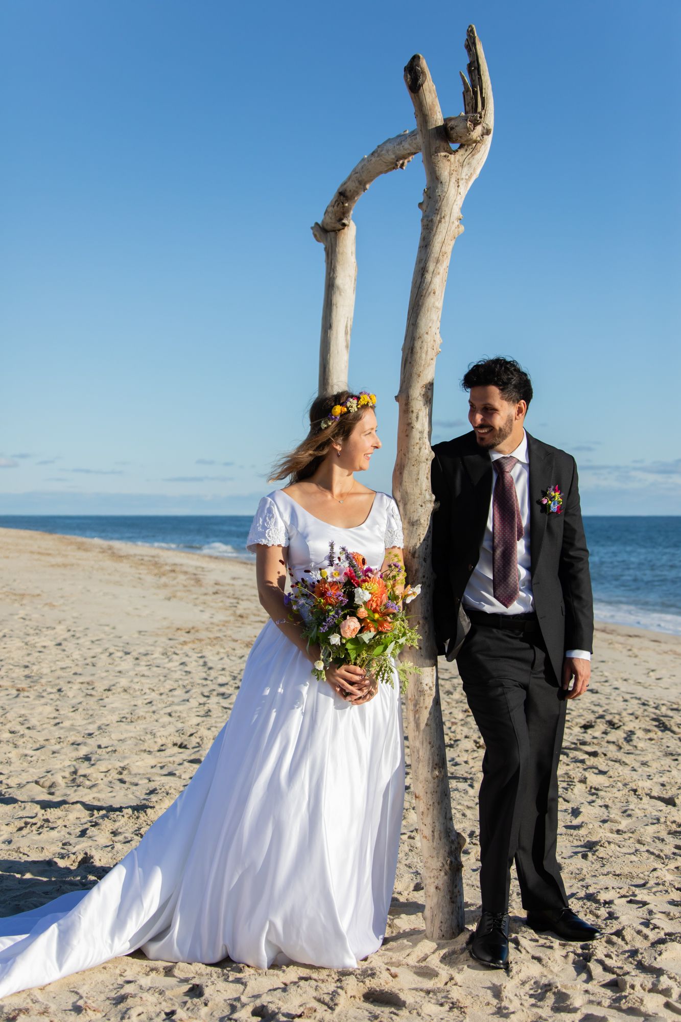 Beach wedding portraits with driftwood arch and natural coastal lighting.
