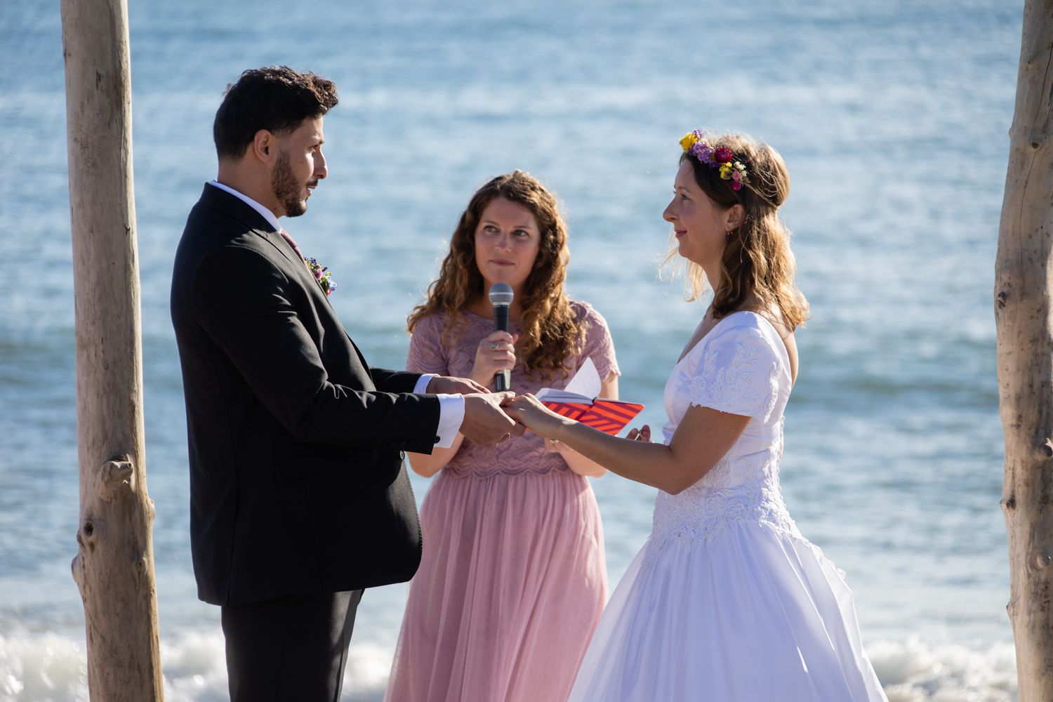 A wedding ceremony taking place under a driftwood arch by the ocean.
