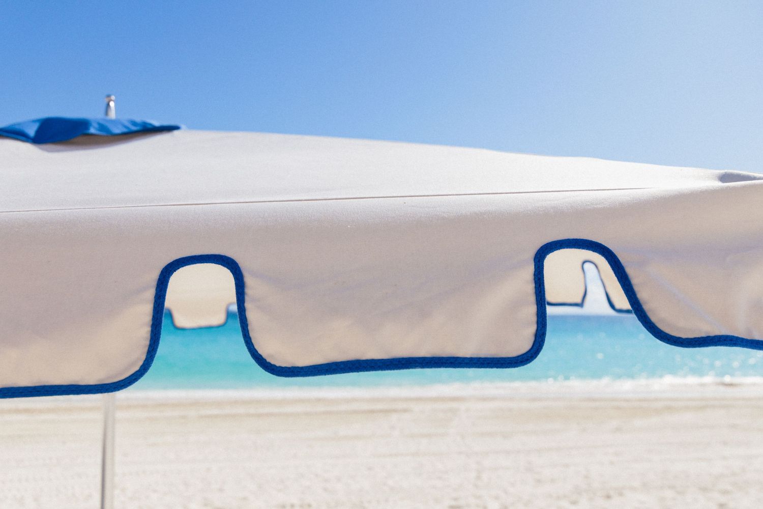Beach umbrella with blue trim creating geometric shapes against bright sky.