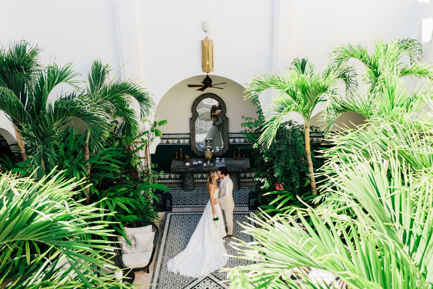 An elegant wedding scene with palm trees framing a Mediterranean-style archway and pathway.