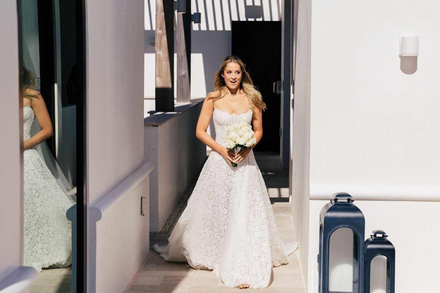 Person in white sparkly dress walks through modern hallway with blue lantern decorations.
