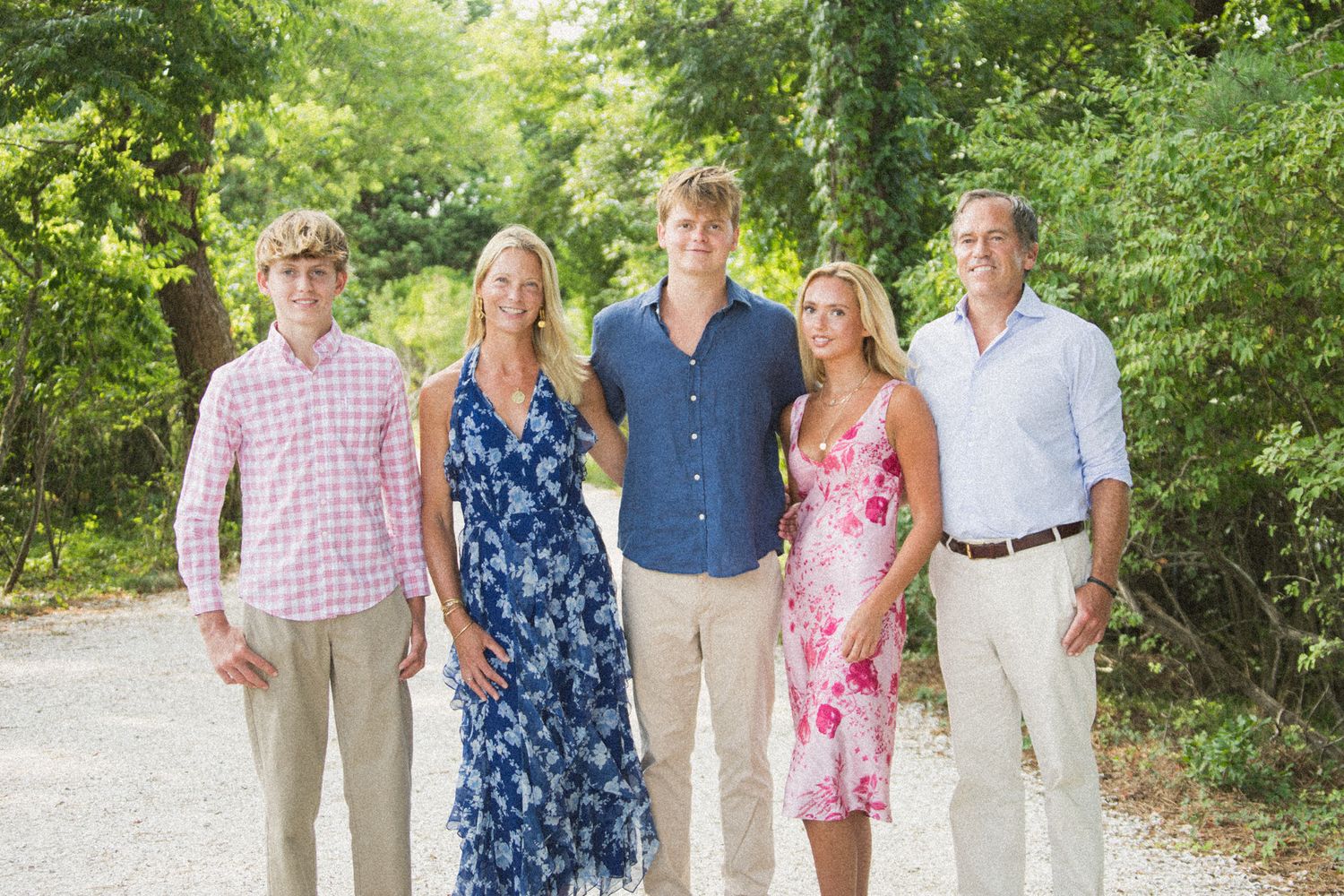 Extended family gathering outdoors in summer casual attire among green foliage.