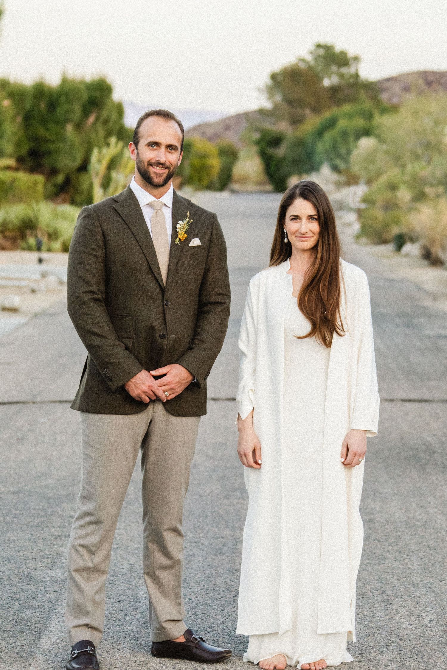 A couple poses for a formal portrait on a road surrounded by desert landscape.