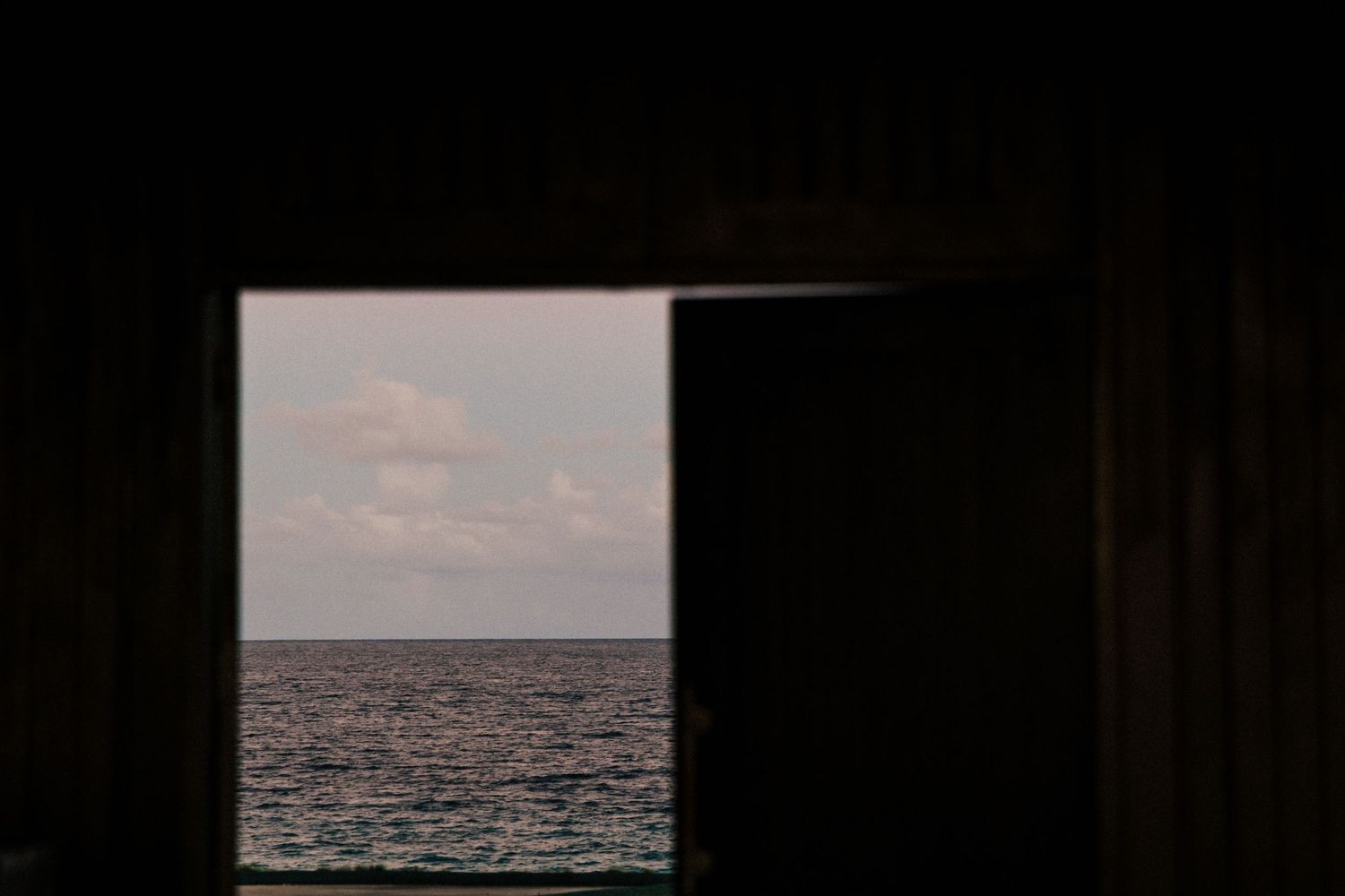 Dark silhouette of doorway framing ocean view at sunset.