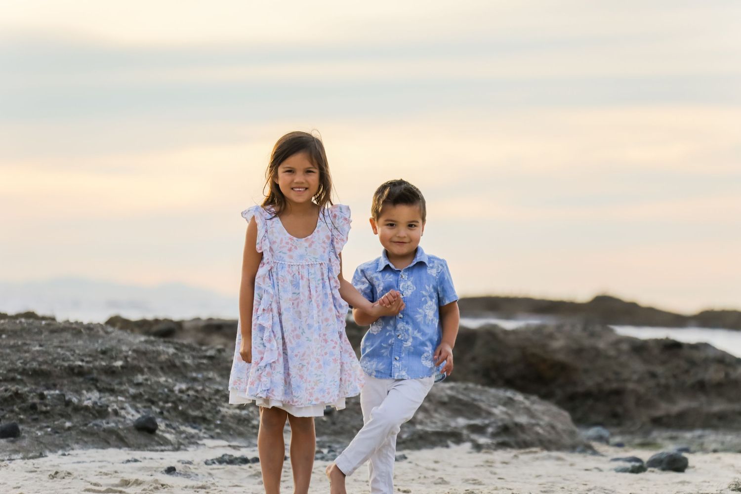 Children playing together on a sandy beach at sunset with rocky coastline in the background.