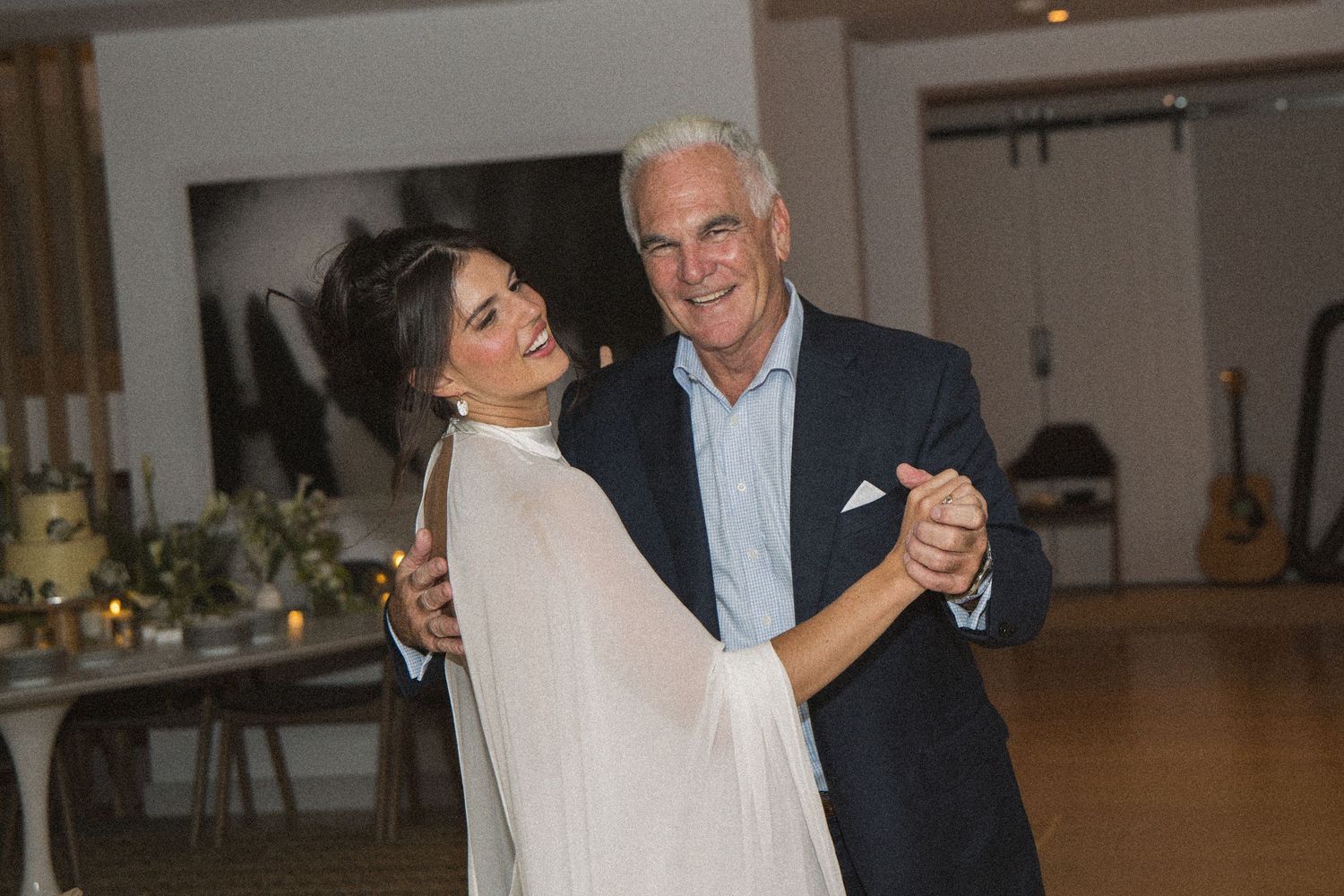Bride and older gentleman share a first dance at an elegant wedding reception in a modern venue.