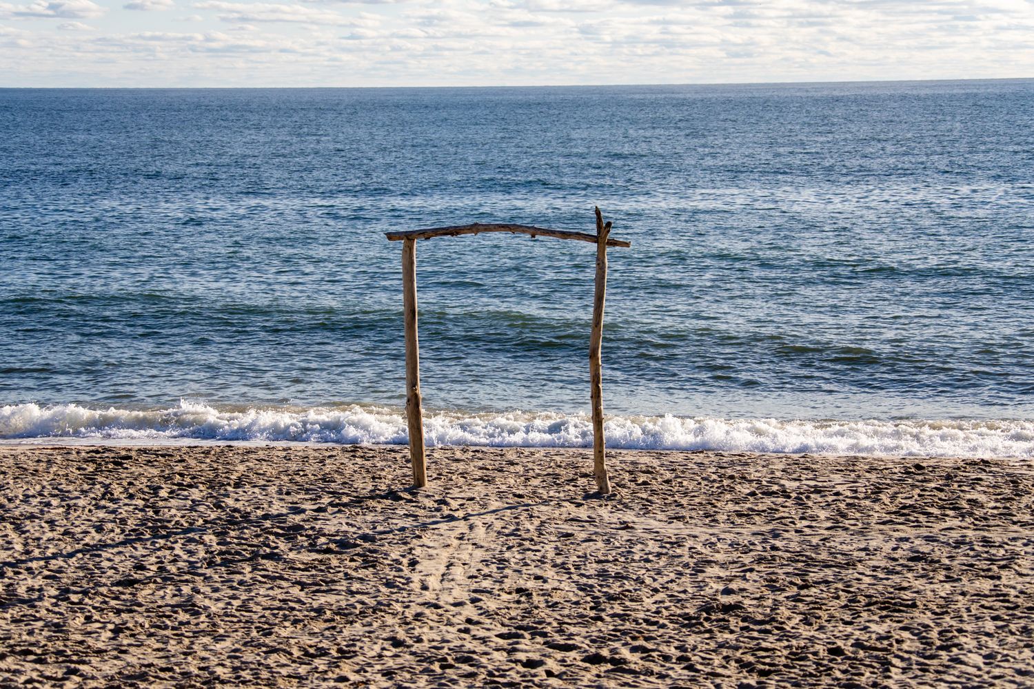 Rustic wooden arch decorated for a beach wedding ceremony against an ocean backdrop.