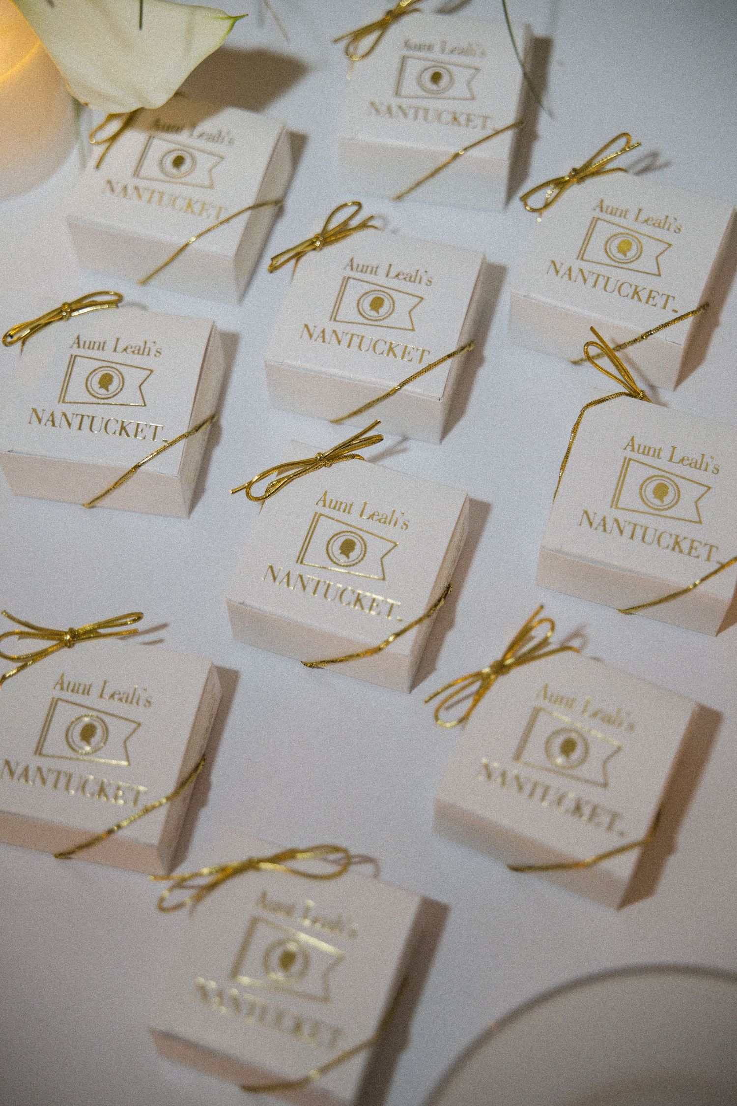 White gift boxes with gold bows and Aunt Leali's Nantucket branding arranged on a table as wedding favors.