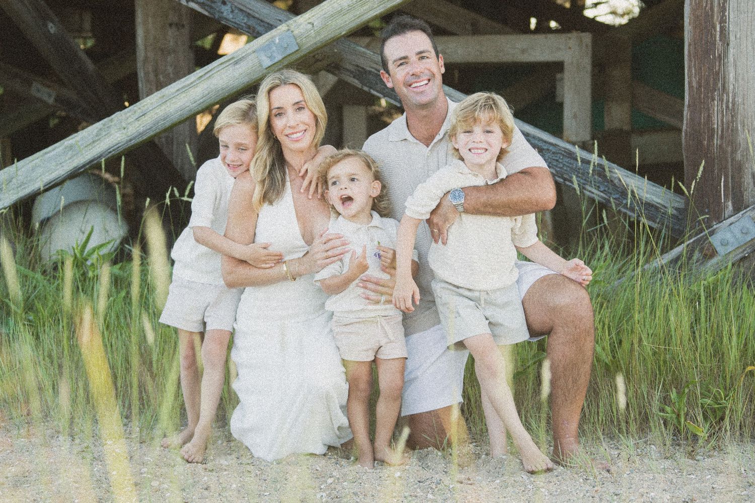 A family in white outfits poses together under a rustic wooden structure in tall grass.
