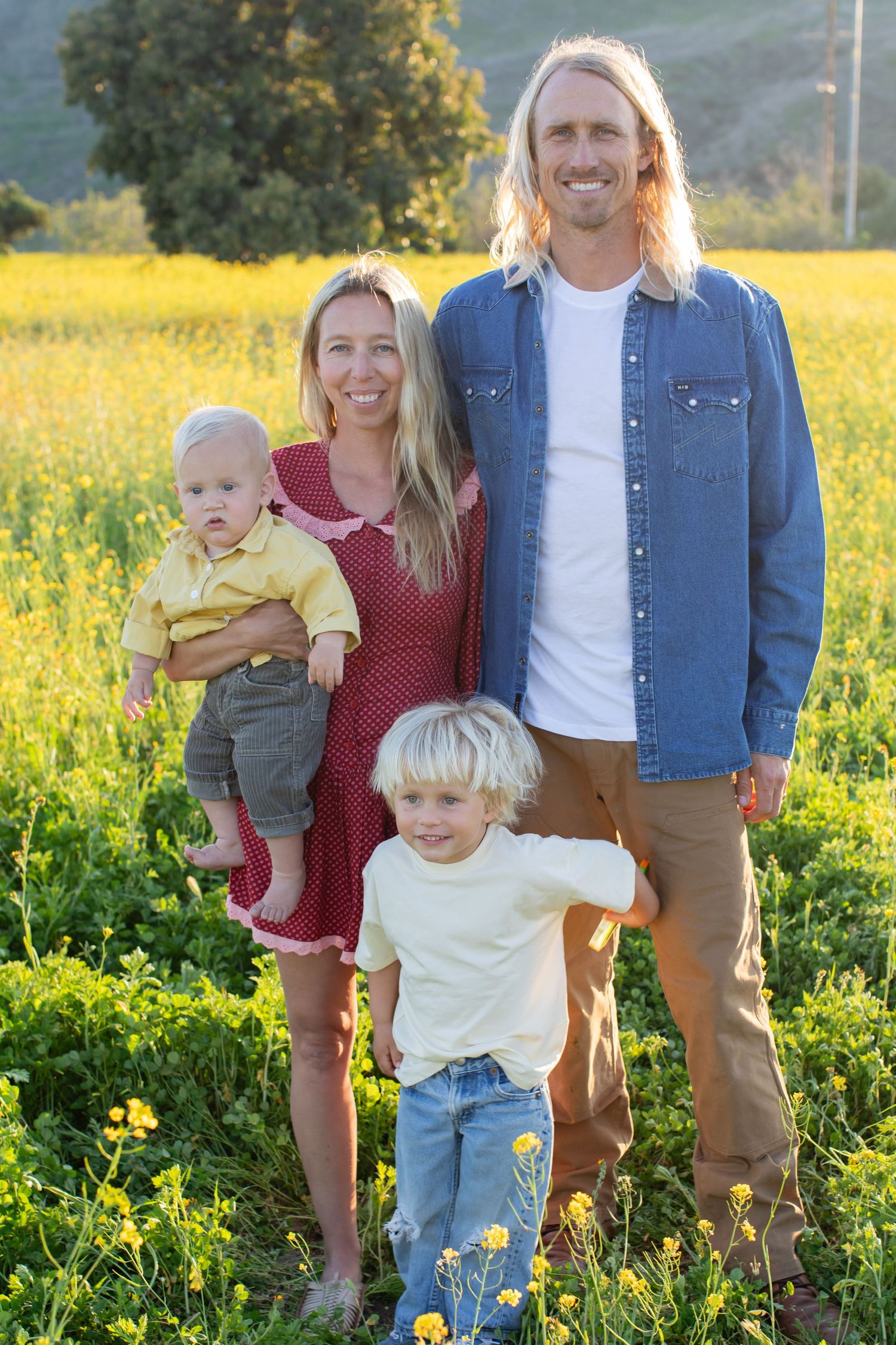 Family group photo in casual attire standing among yellow wildflowers with mountains in background.