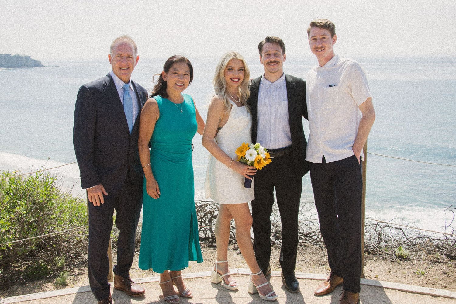 Family and friends pose together at a seaside wedding celebration.