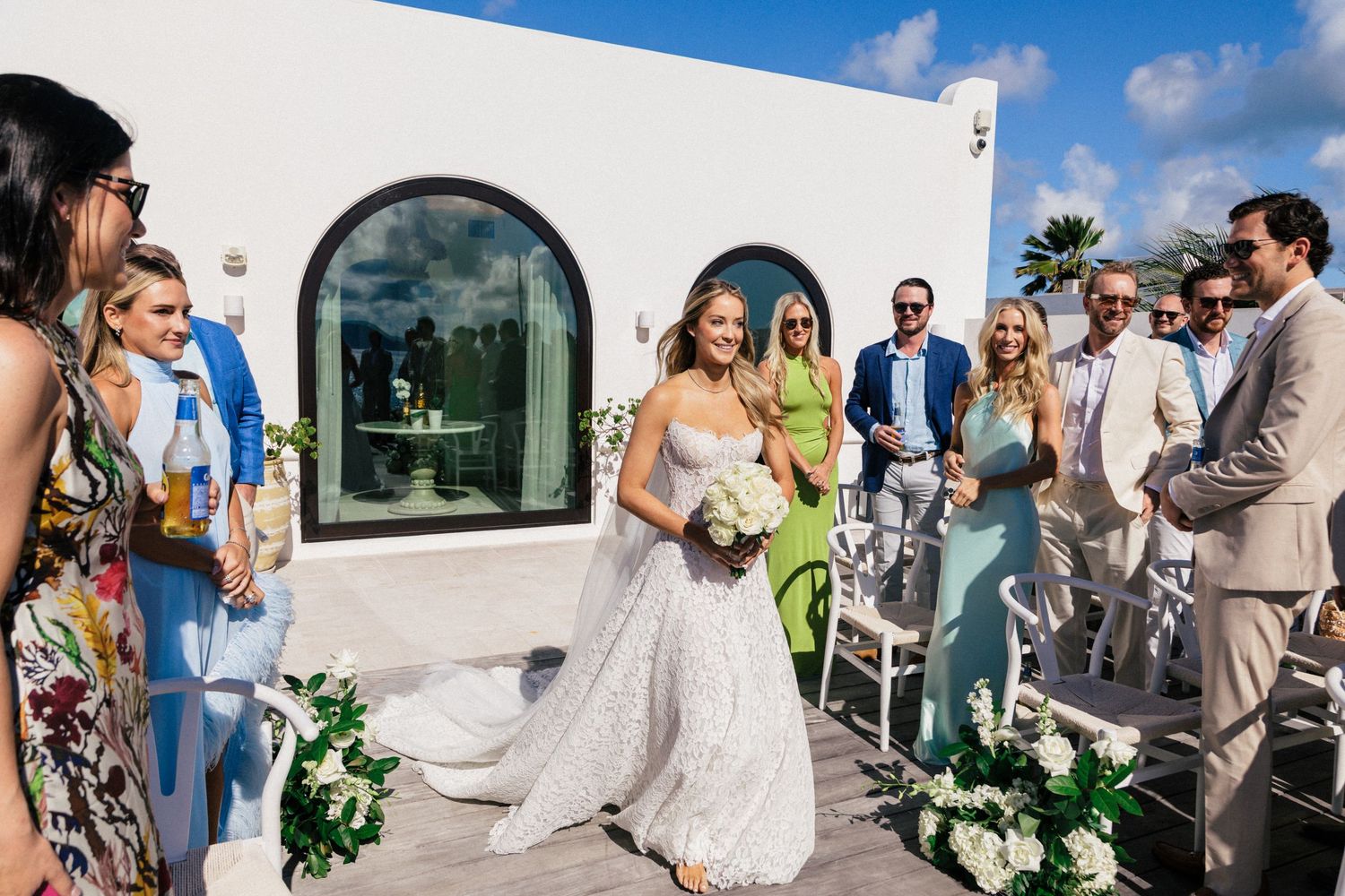 Wedding ceremony guests gathered on white terrace with arched windows and ocean views.