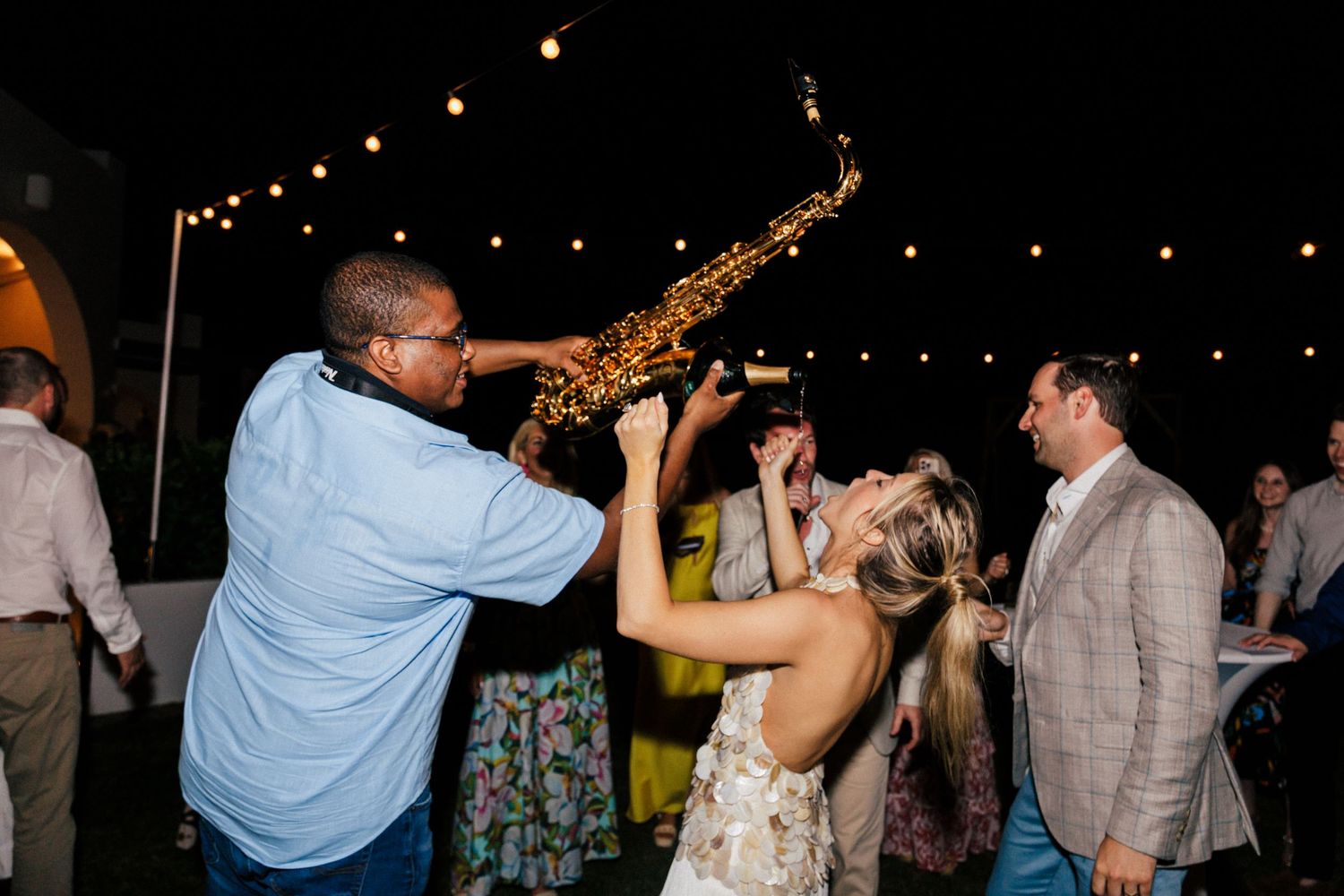 Guests dancing and celebrating at a festive outdoor reception with string lighting overhead.