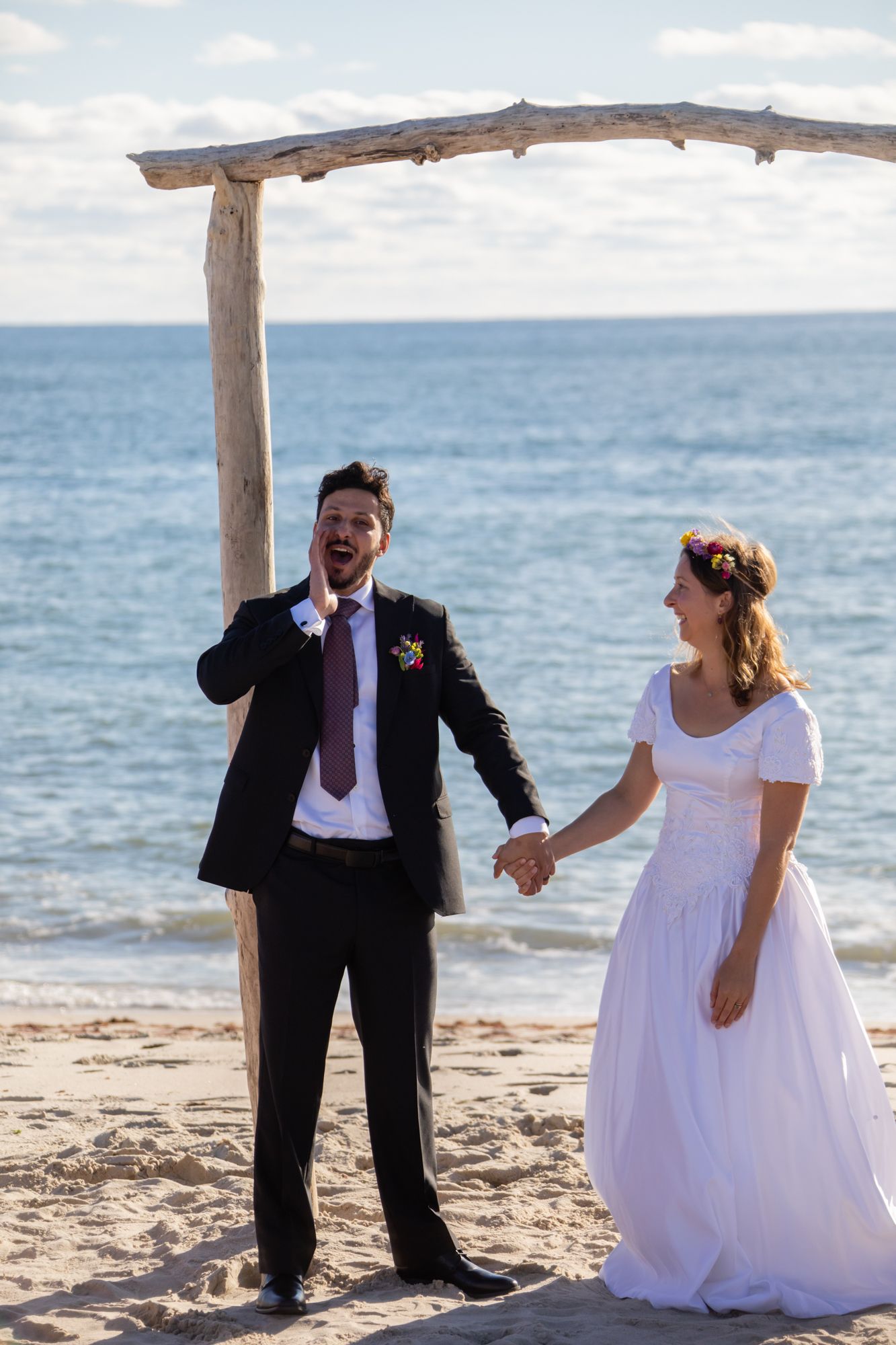 A joyful beach wedding ceremony with a couple posing playfully in front of the ocean.