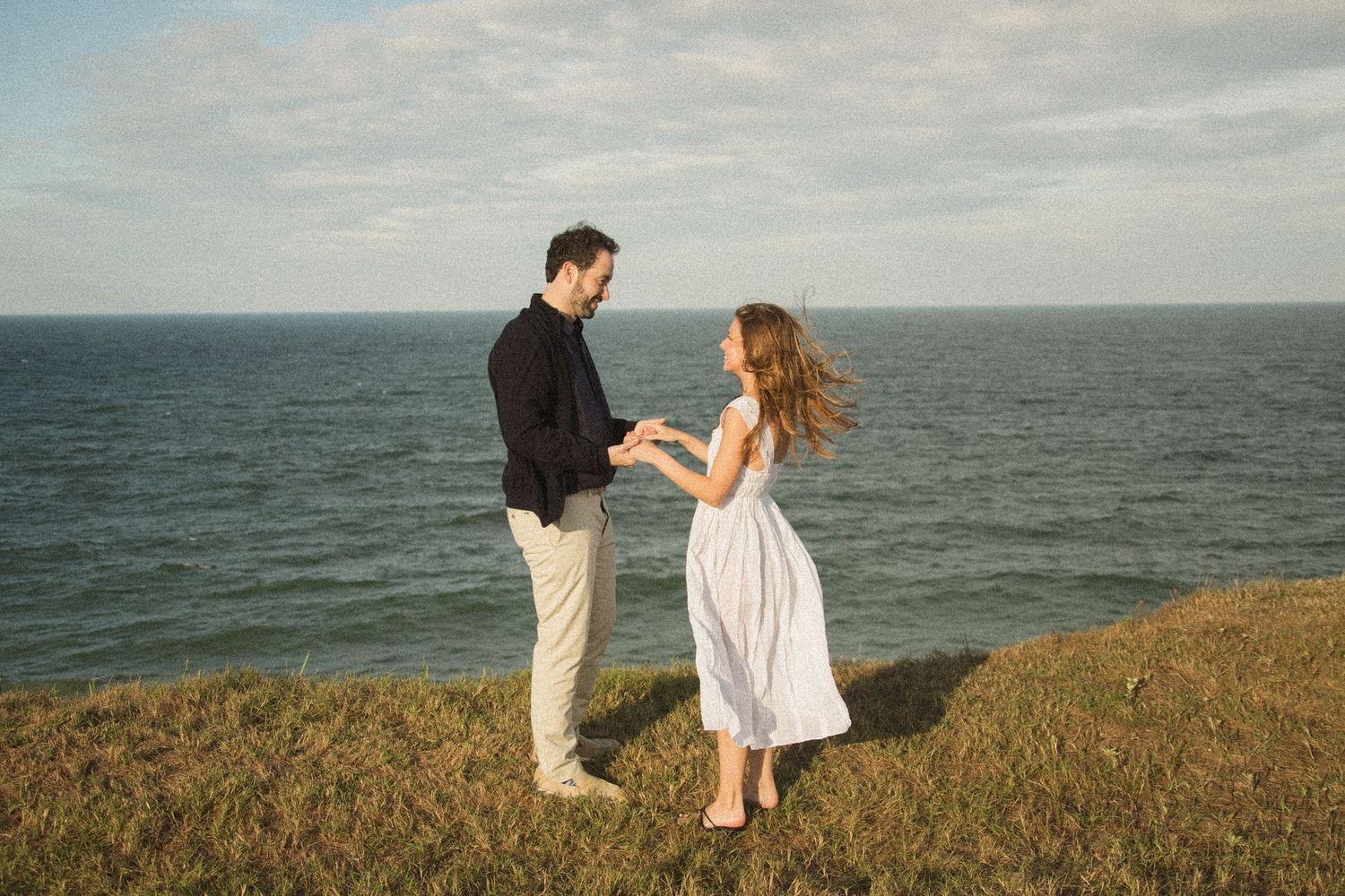 A couple dances on a cliff edge with the vast ocean as their backdrop.