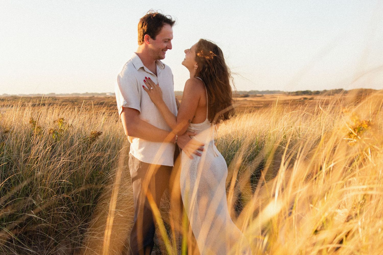 Couple embracing in golden wheat field during sunset photoshoot.