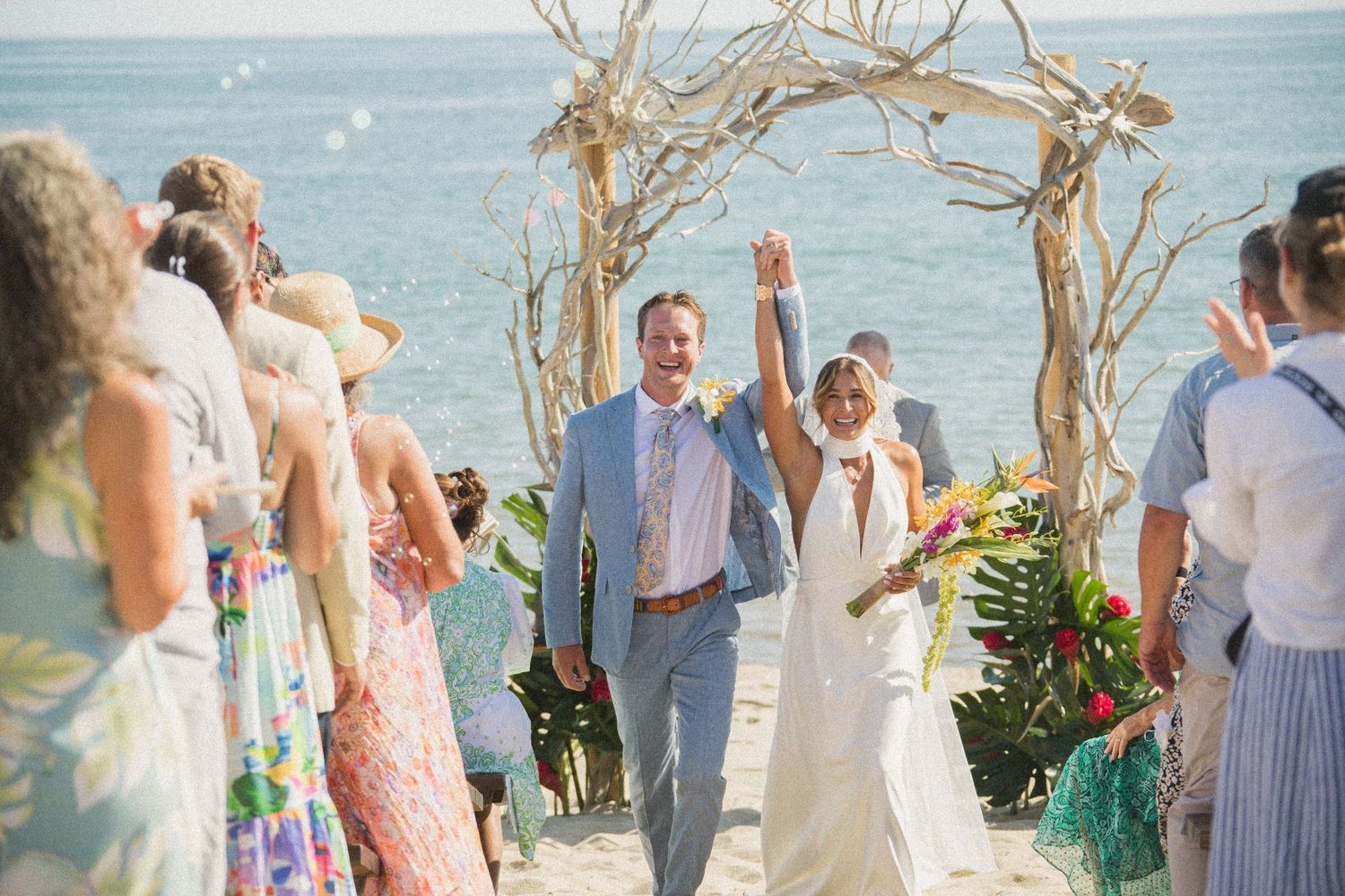 Wedding party and guests celebrating on beach after ceremony.