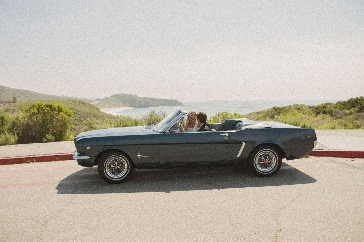 Classic vintage Mustang convertible parked on a scenic coastal road.