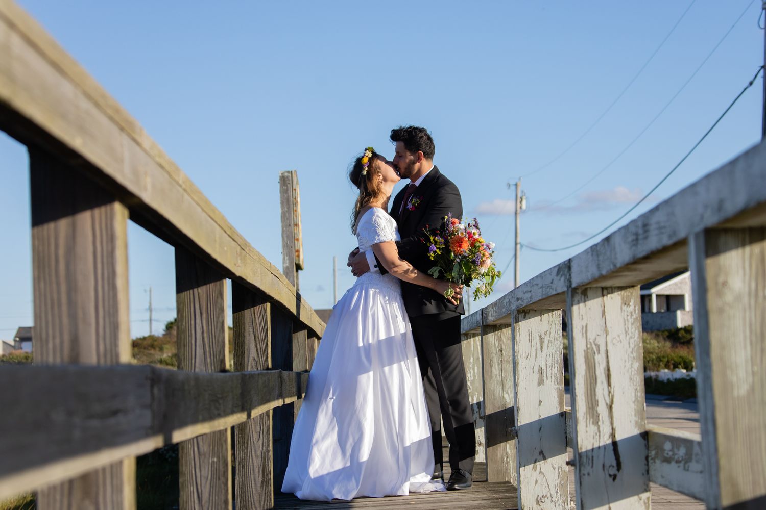 Newlyweds posing on a wooden boardwalk with coastal scenery.