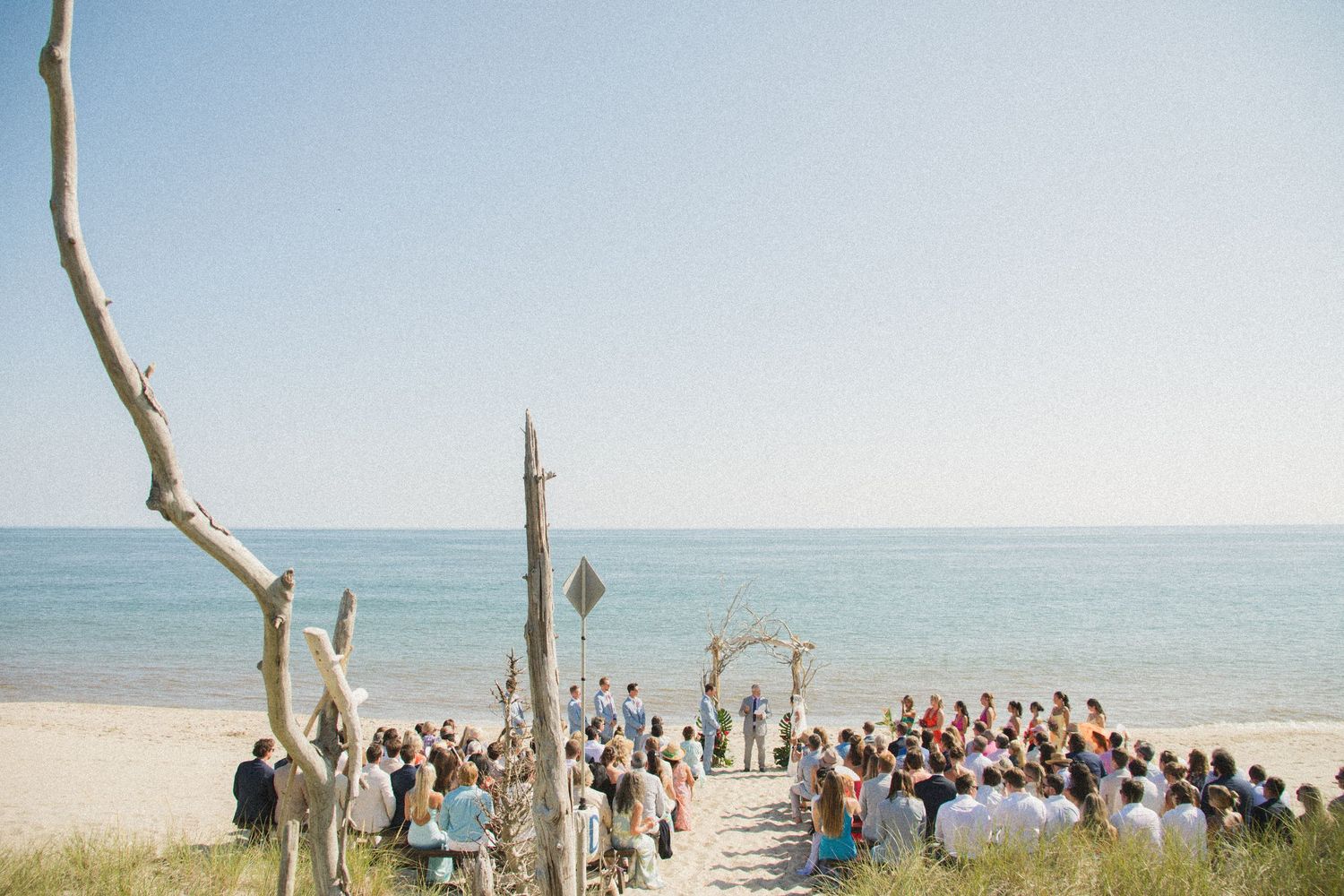 Wide angle view of beach wedding ceremony with guests seated along shoreline.
