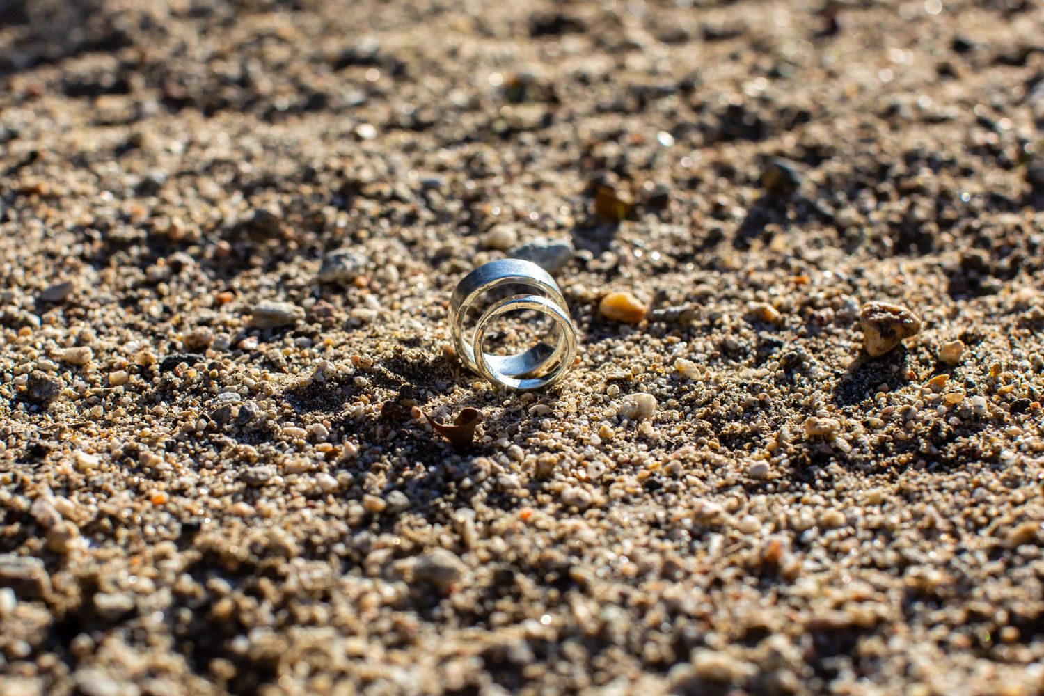Wedding rings nestled in sandy soil captured in macro photography.