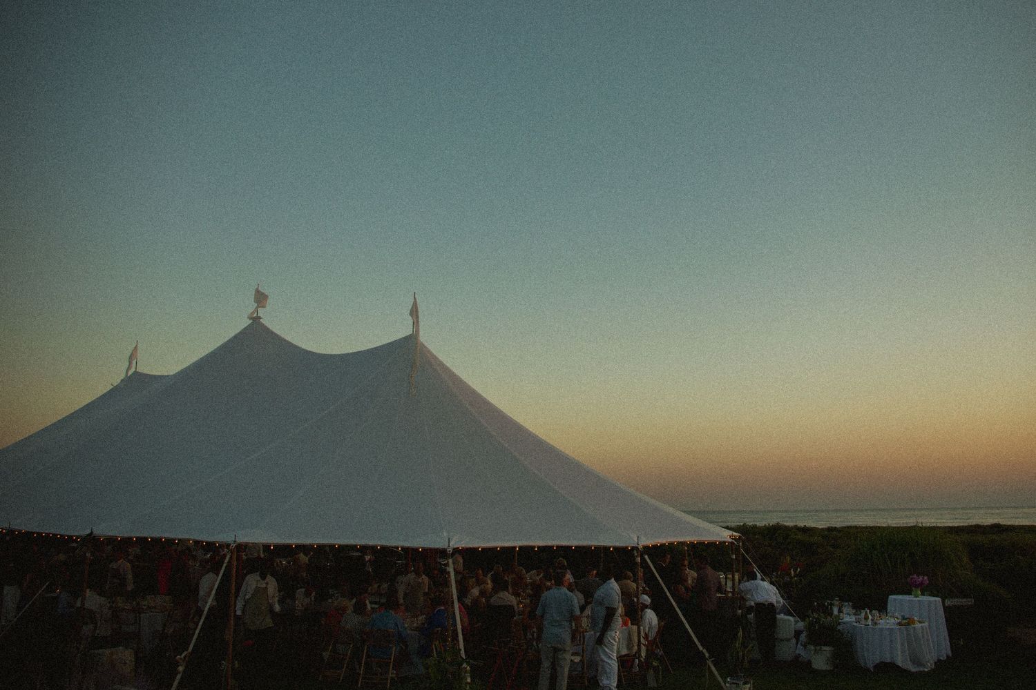 Large white event tents silhouetted against a sunset sky at an outdoor venue.