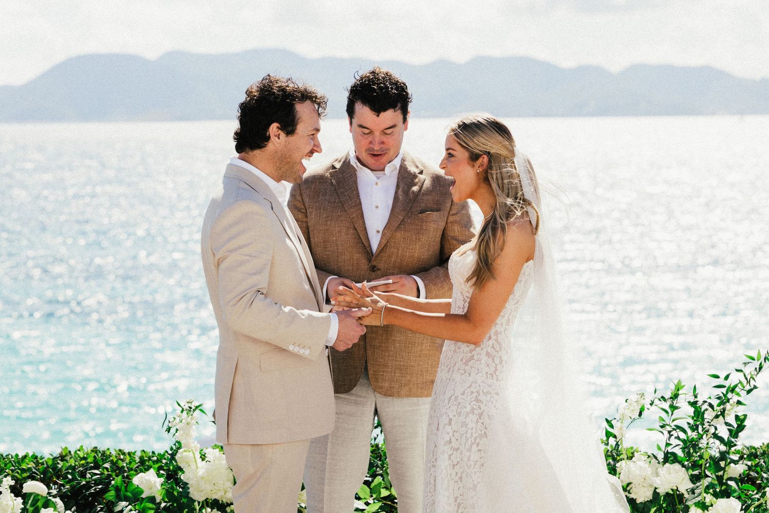 Romantic beach wedding ceremony with couple and guests celebrating by the ocean at sunset.