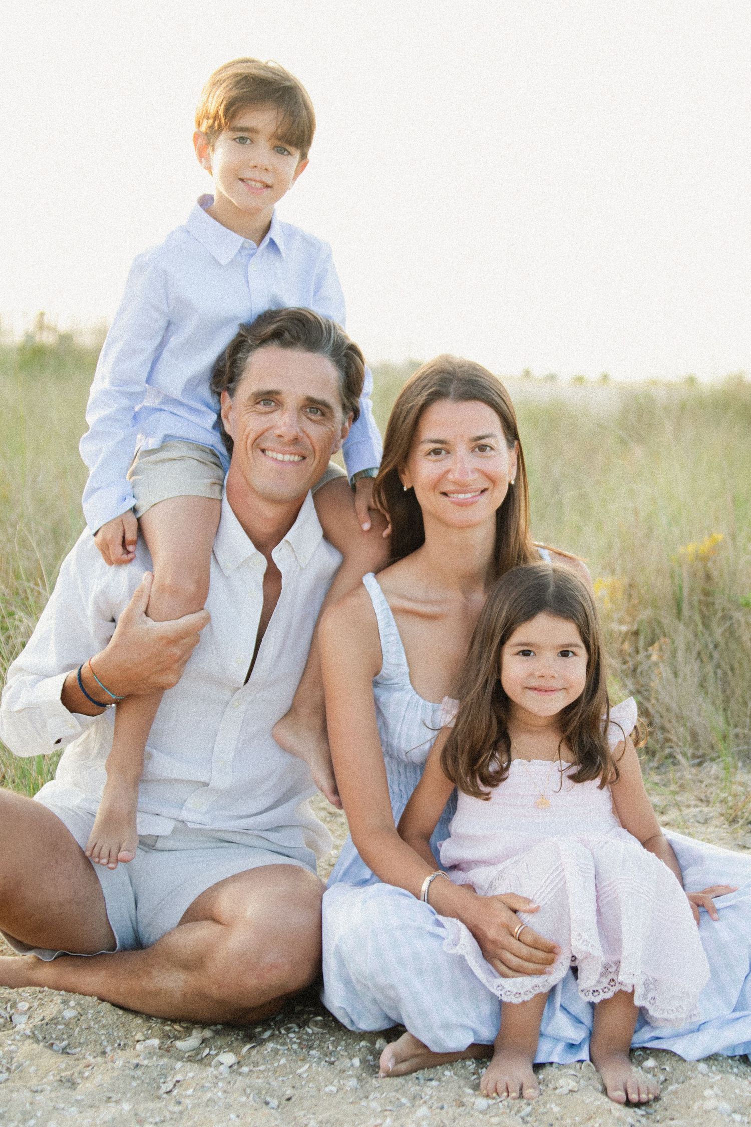 Casual beach portrait session with family sitting together in white and blue outfits.