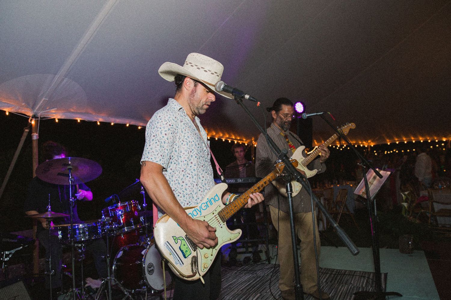 Band performing on stage at an outdoor event with musical instruments and lighting equipment.