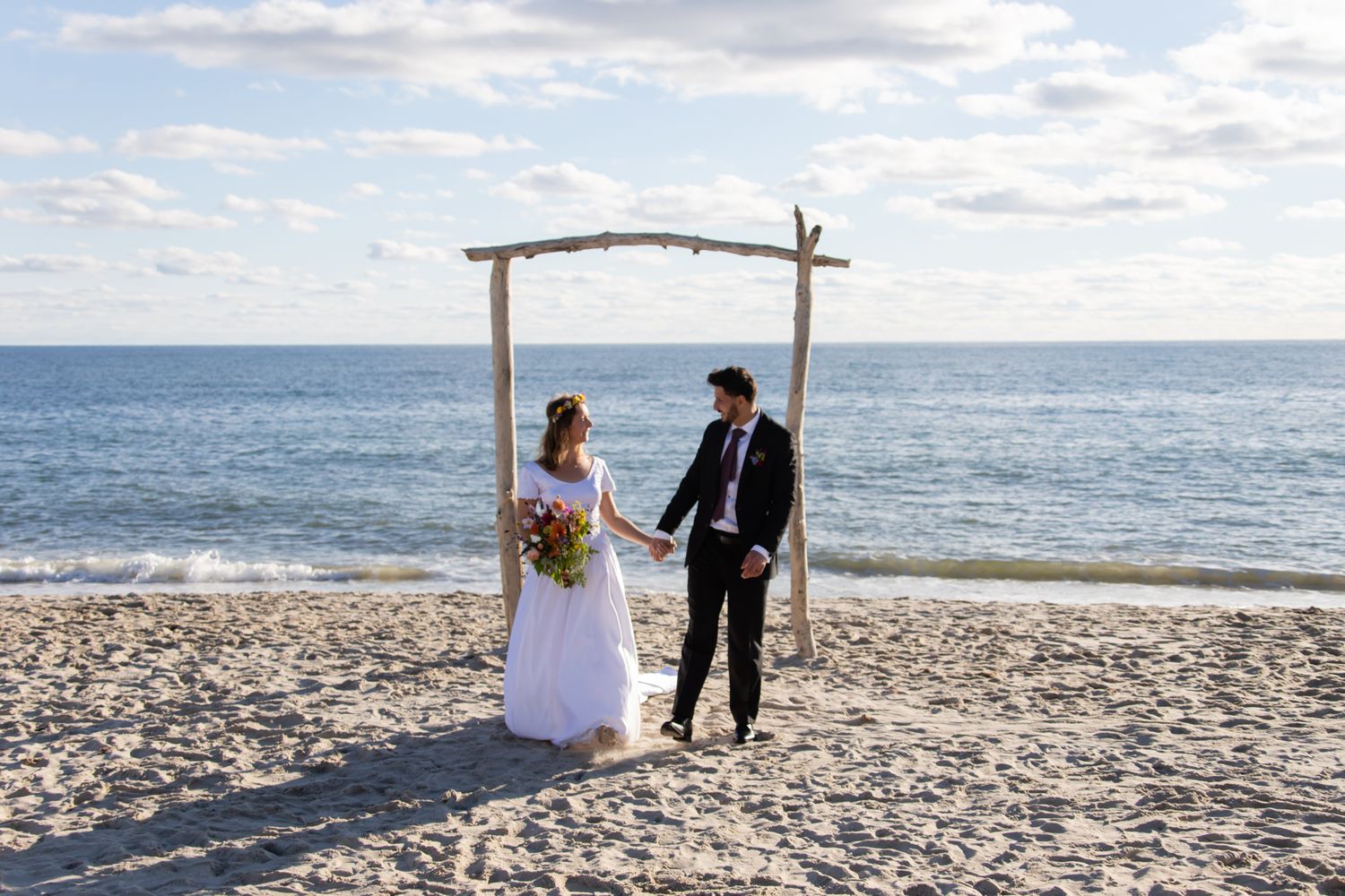 A romantic beach wedding ceremony setup with a wooden arch and floral arrangements on a sandy shoreline.