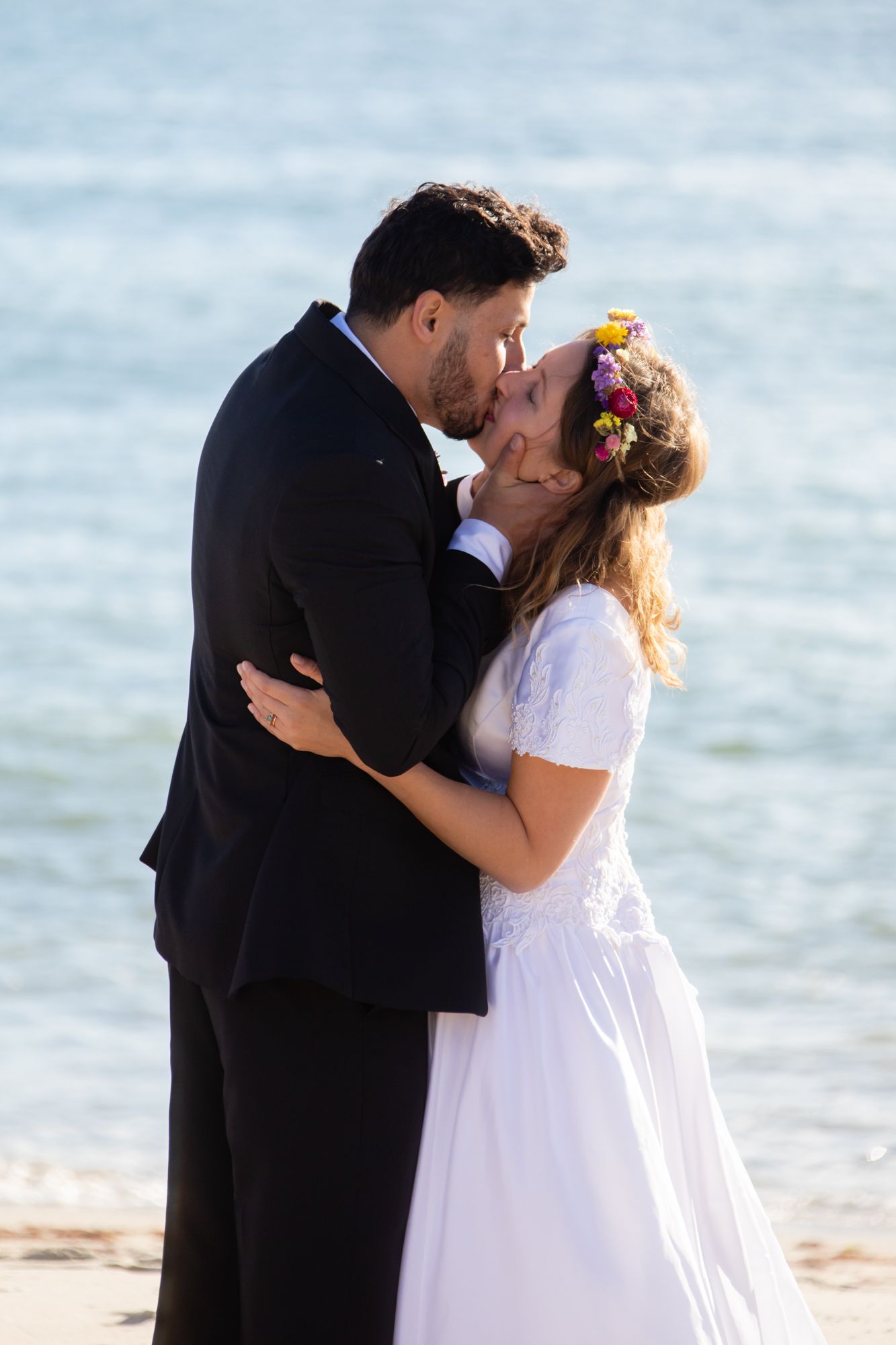 A romantic moment shared between newlyweds on the beach with ocean in background.