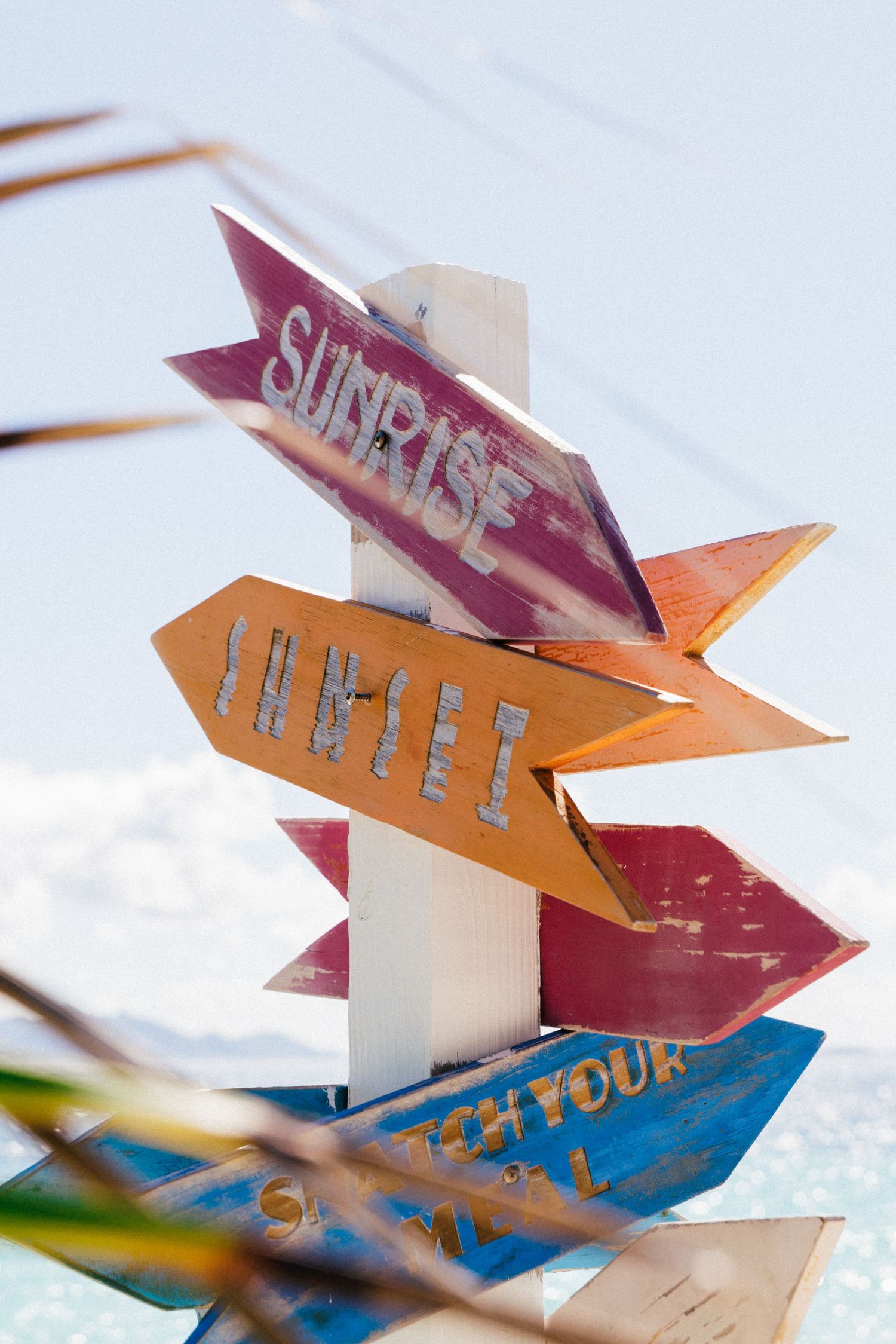 Colorful directional beach signs pointing different ways against bright sky.