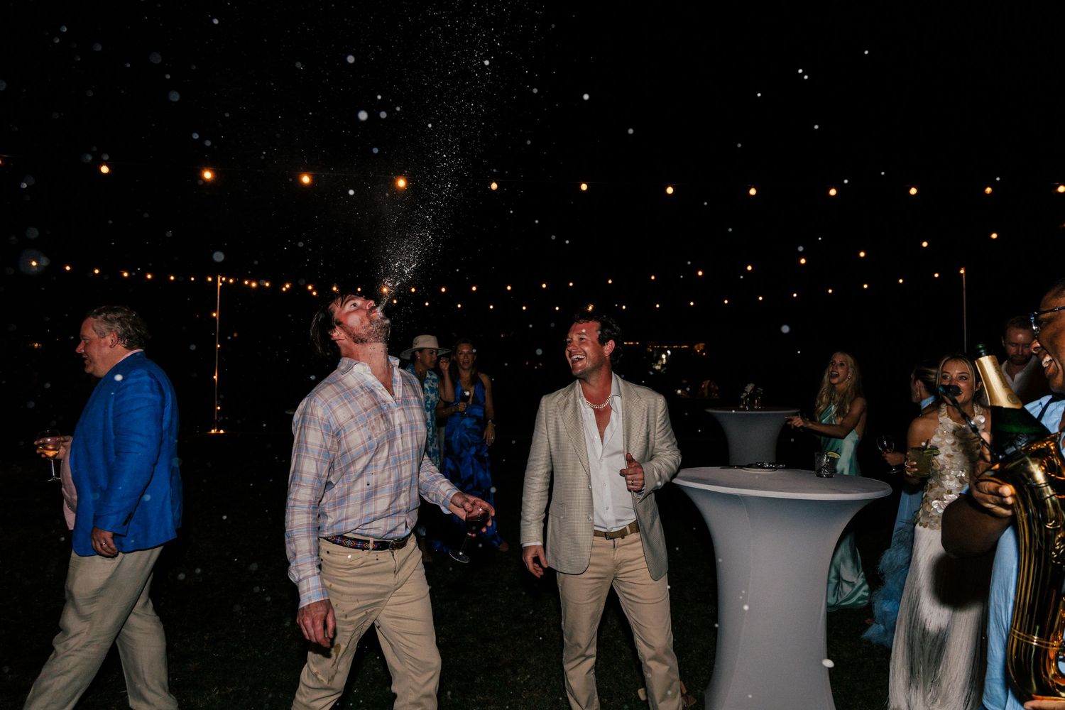 Wedding guests enjoying themselves on an outdoor dance floor illuminated by string lights.