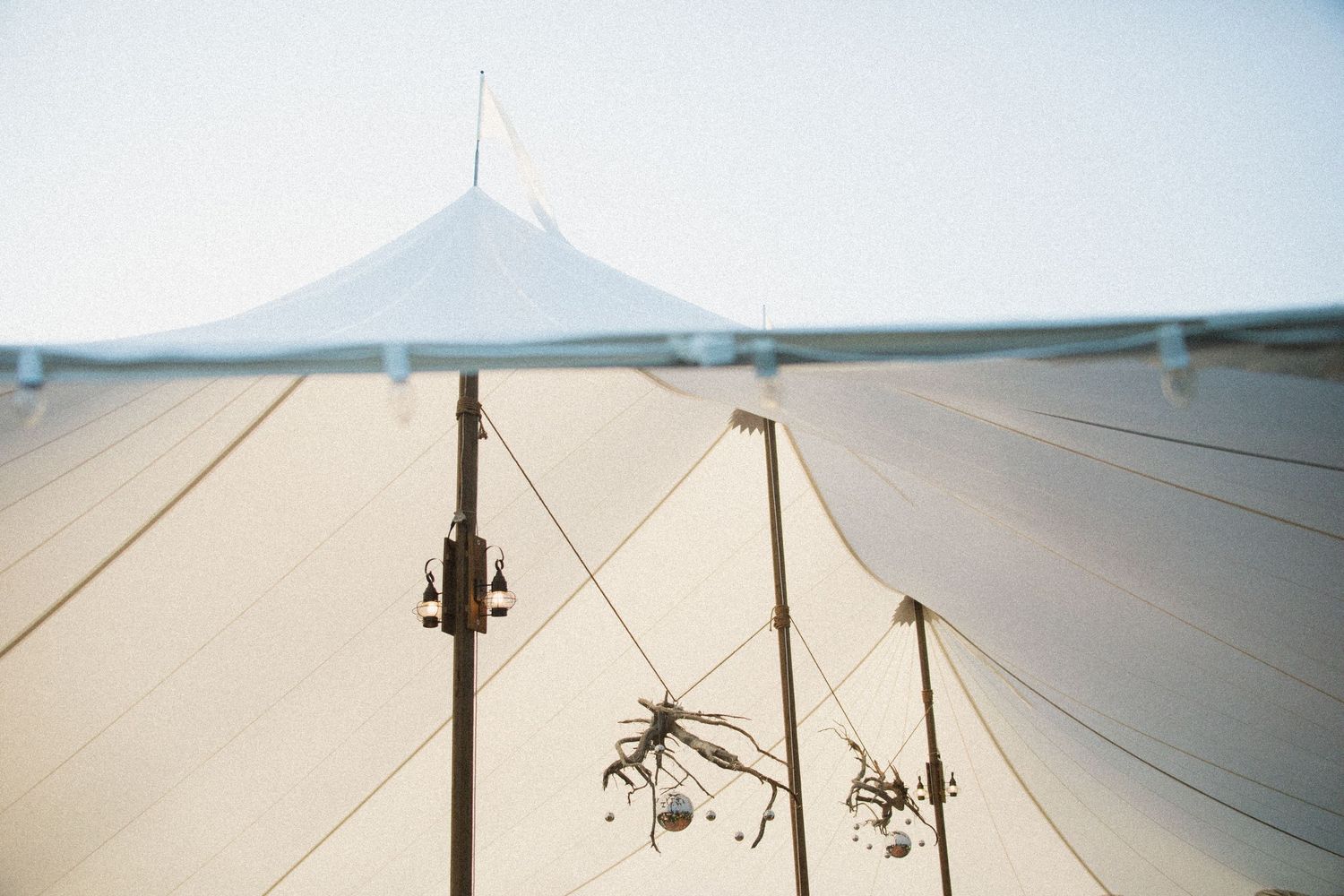 White wedding tent canopy with decorative hanging elements silhouetted against a bright sky.