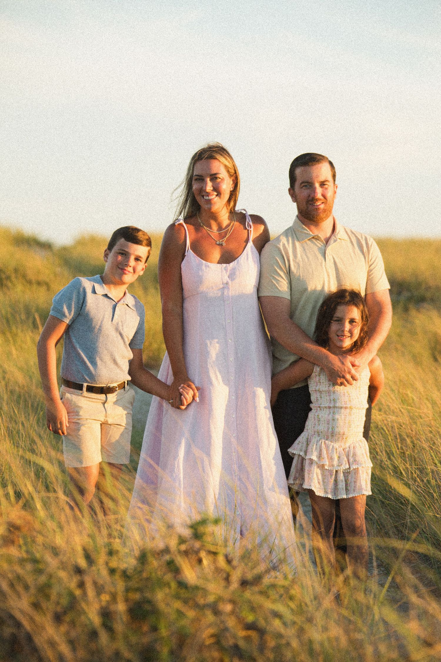 A family stands together in golden beach grass during sunset.