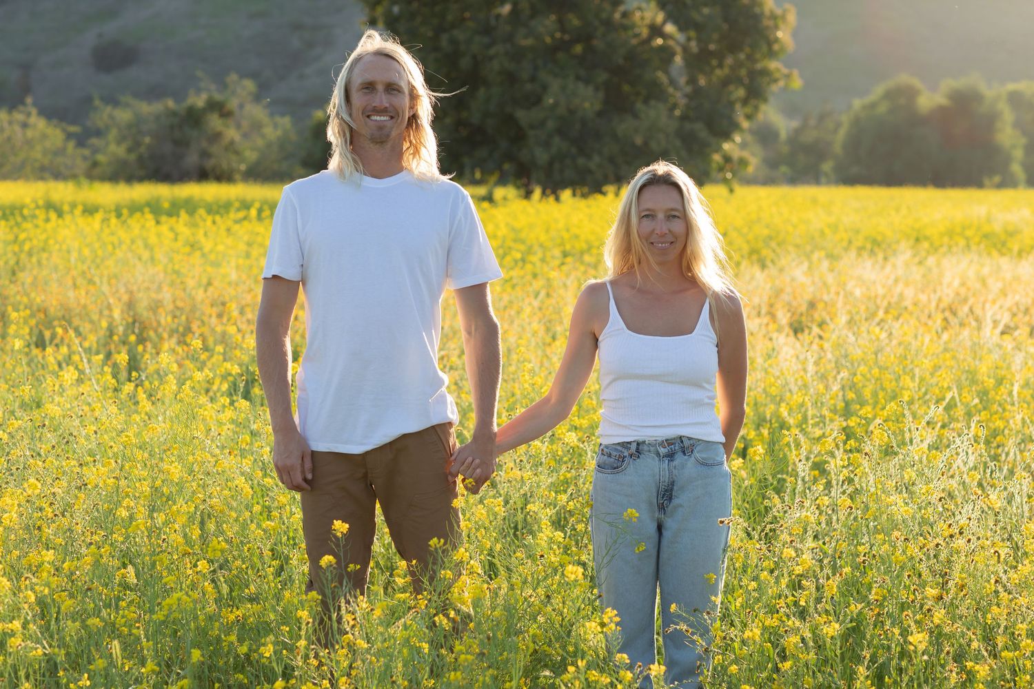 People standing together in a meadow of yellow wildflowers during sunset.