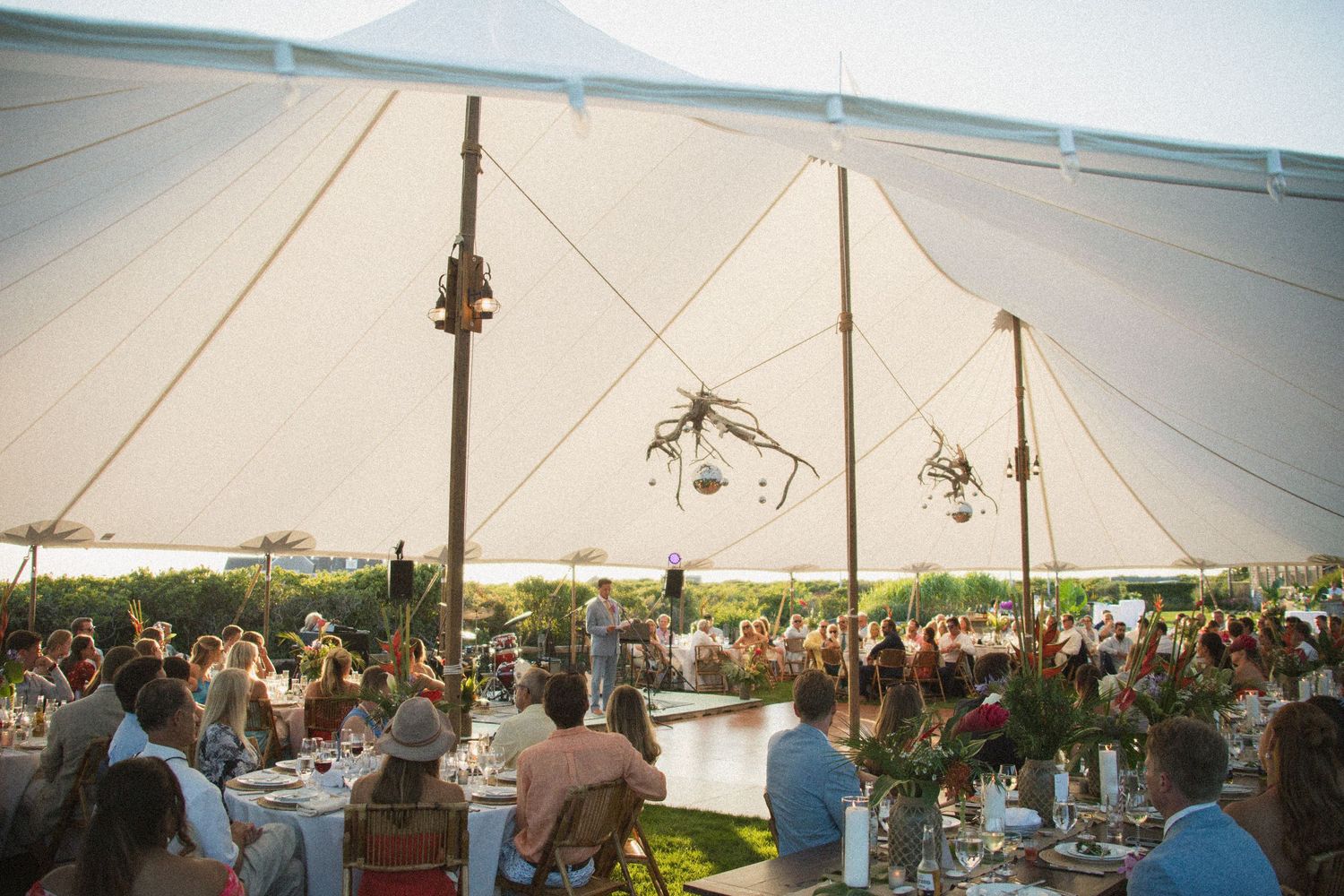 White reception tent decorated with hanging lights and filled with dining tables.