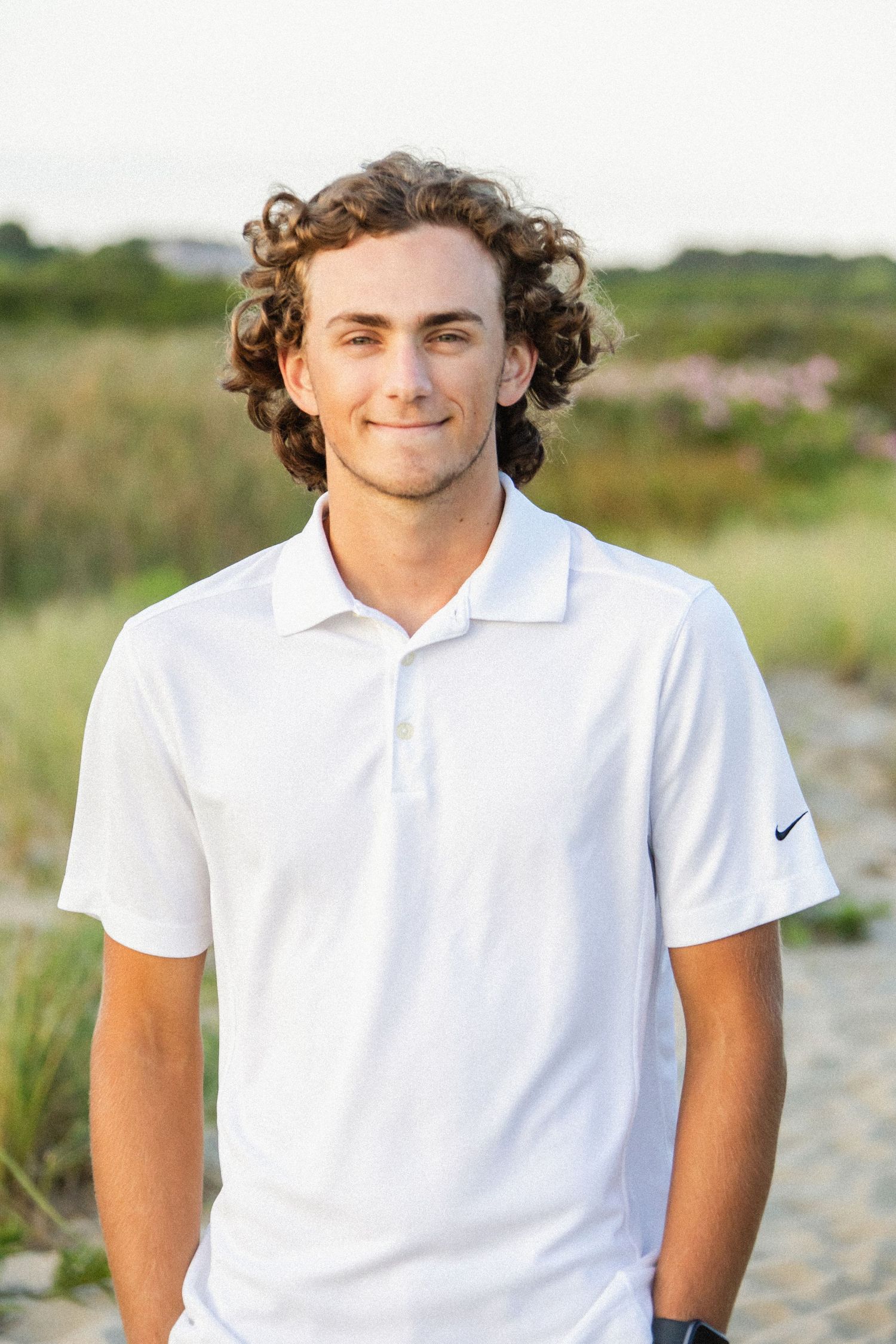 Summer portrait series in white polo shirt against natural coastal background.