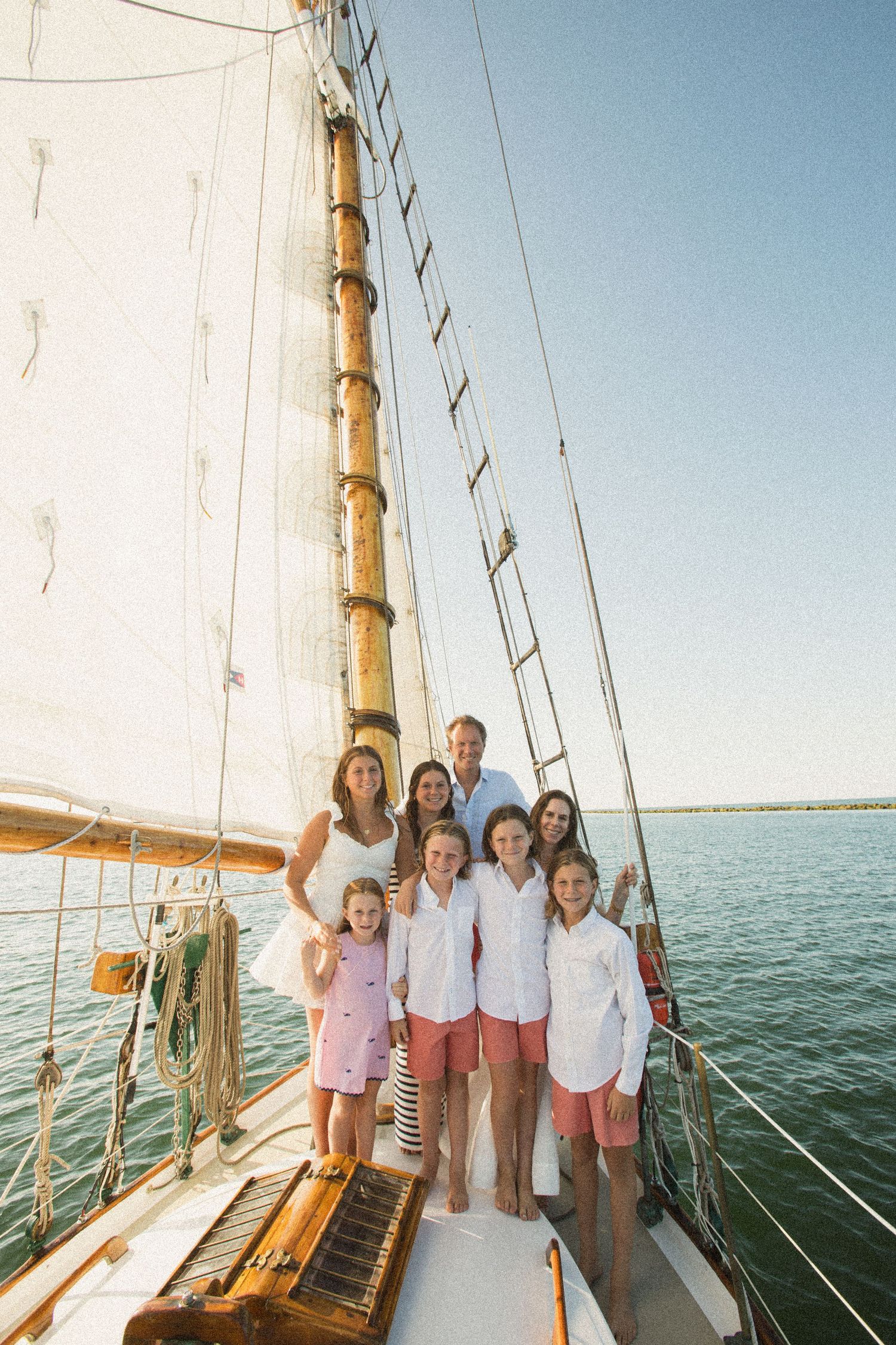Group enjoying a sailing adventure on a classic wooden sailboat against blue waters.