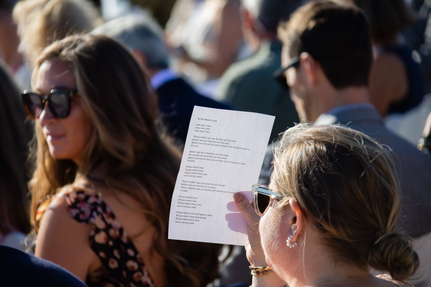 Wedding guests reading ceremony programs during an outdoor beach celebration.