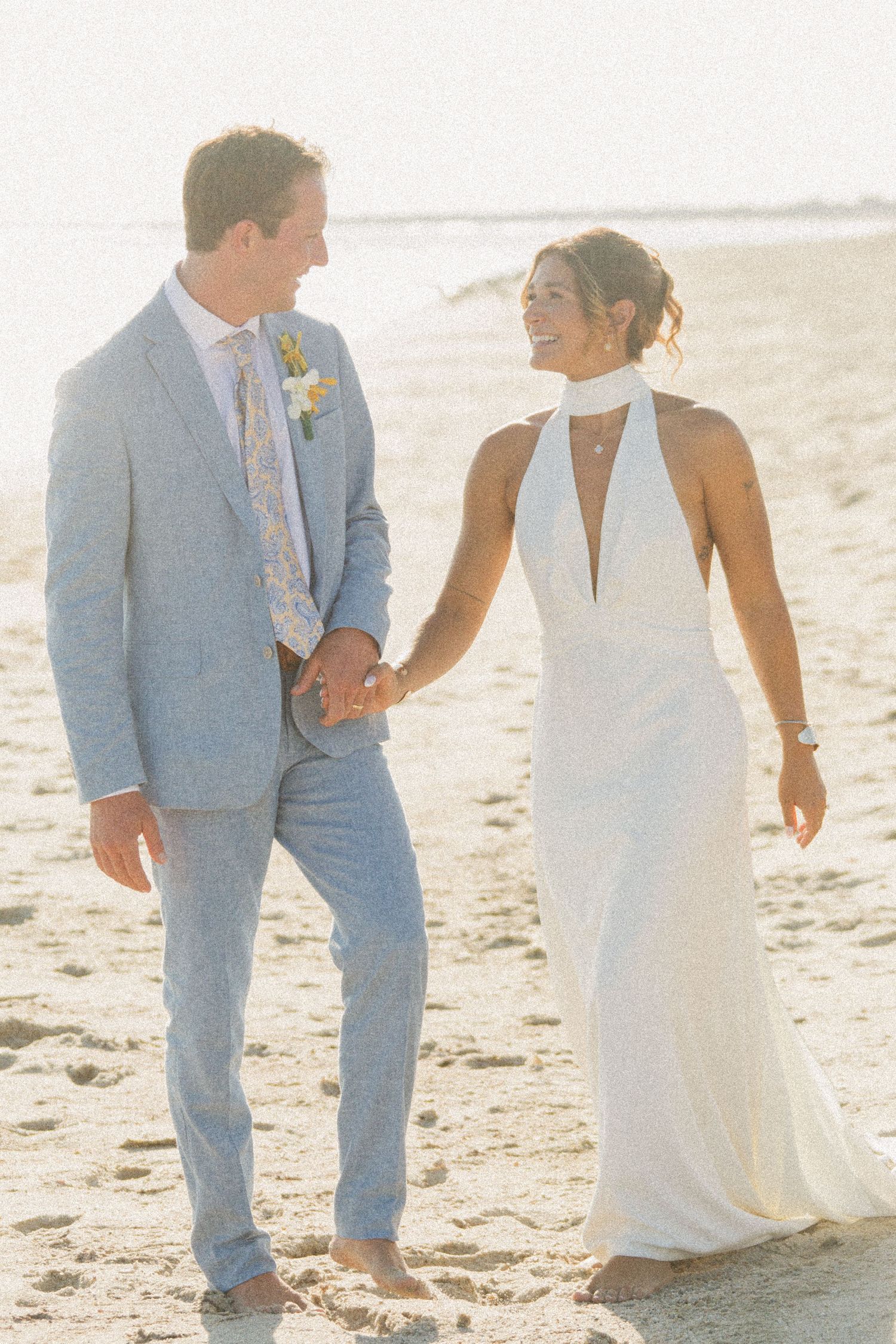 Romantic beach wedding portrait with couple walking hand in hand at sunset.