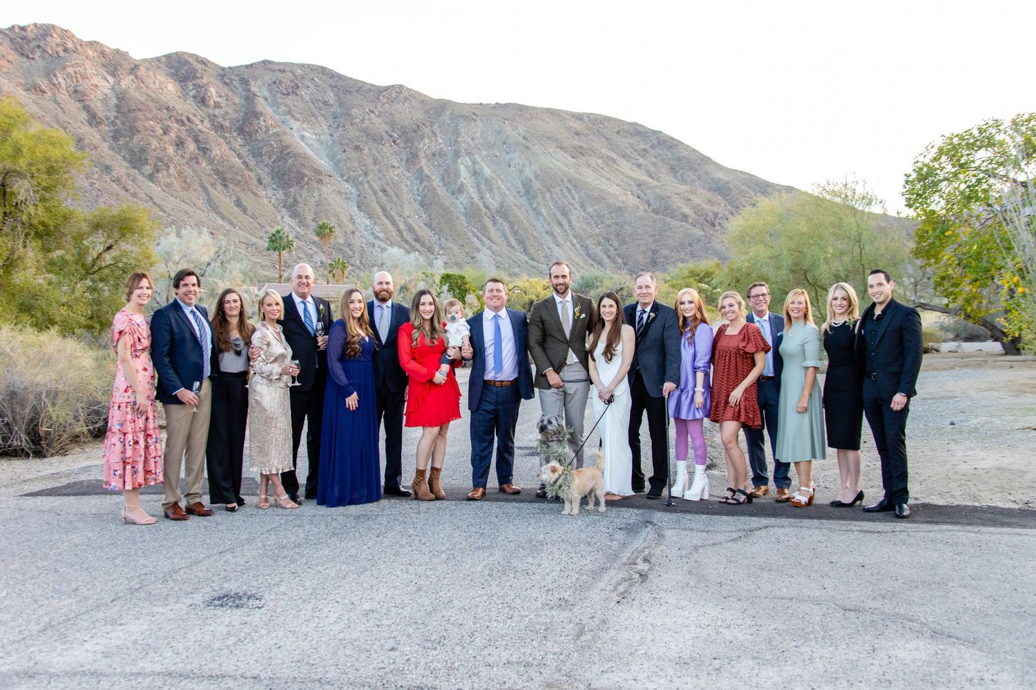 Large group photo of wedding guests posing together against a desert mountain backdrop.