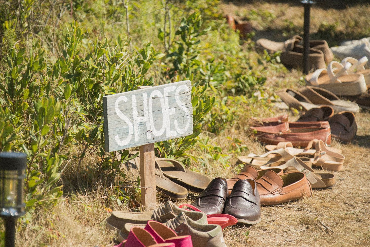 Collection of wedding guests' shoes arranged outdoors on natural ground.